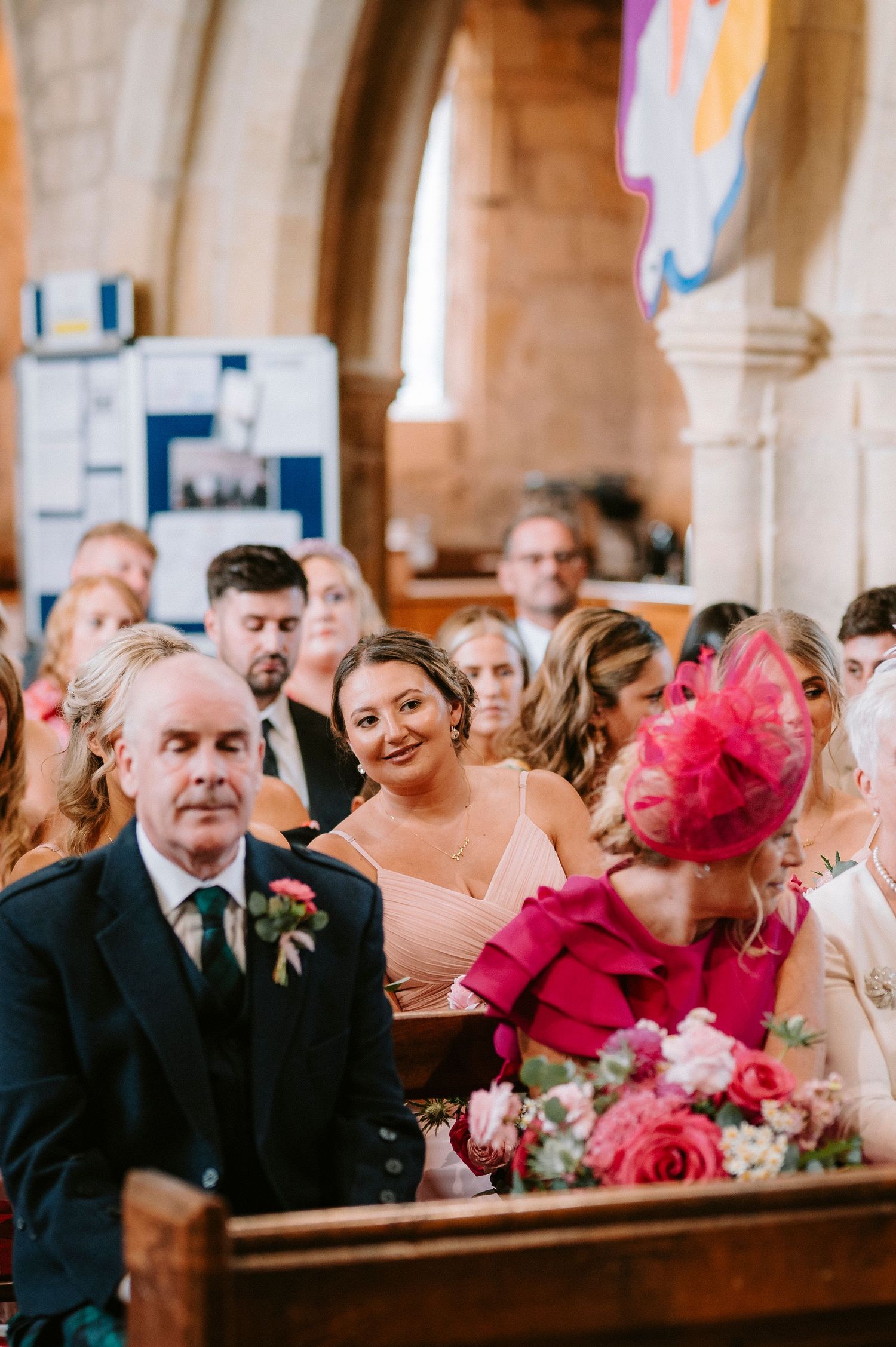 Wedding guests in formal attire seated in church pews with bright pink accents.