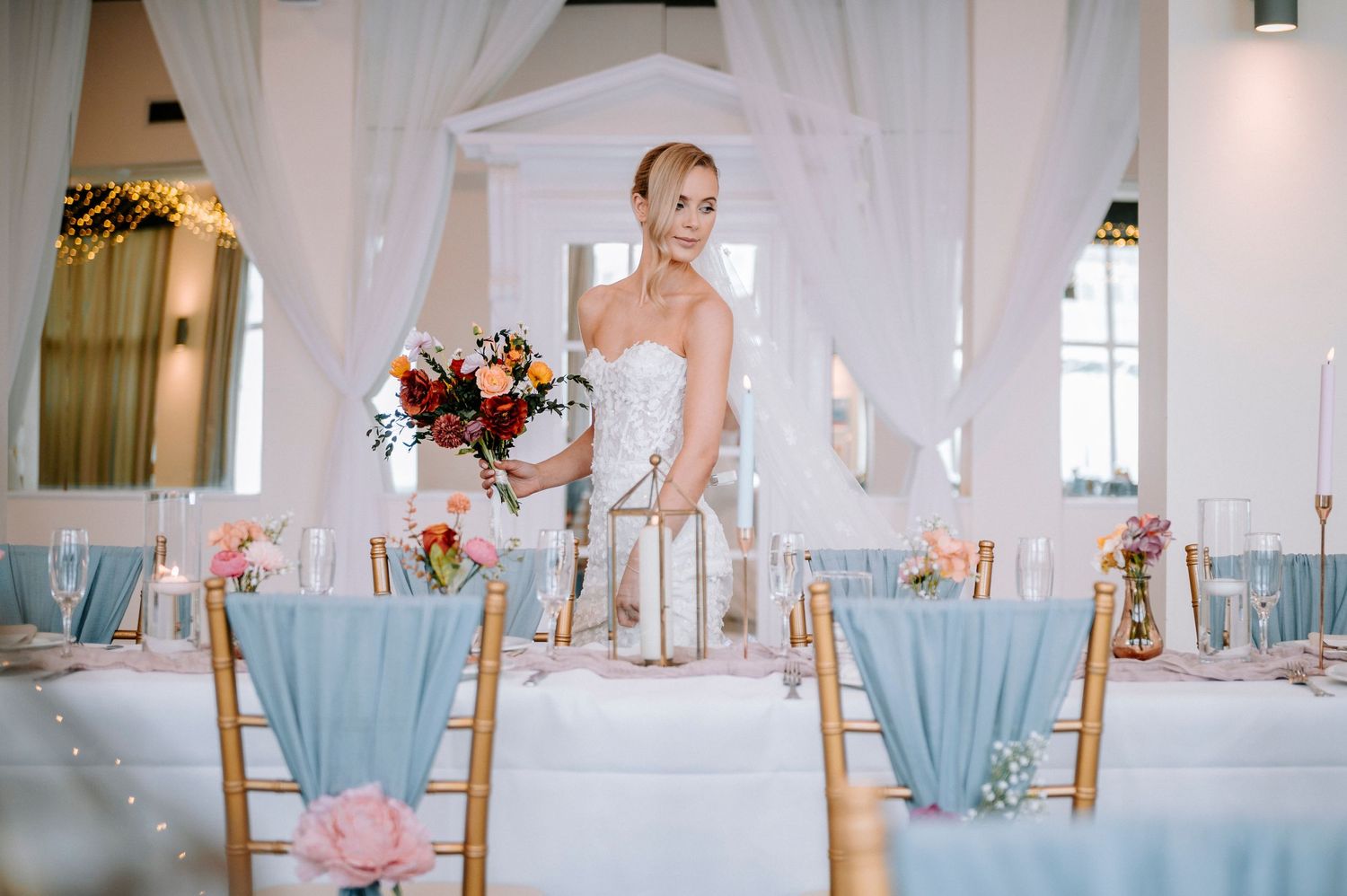 Wedding reception room with white draping and blue accents on dining chairs.