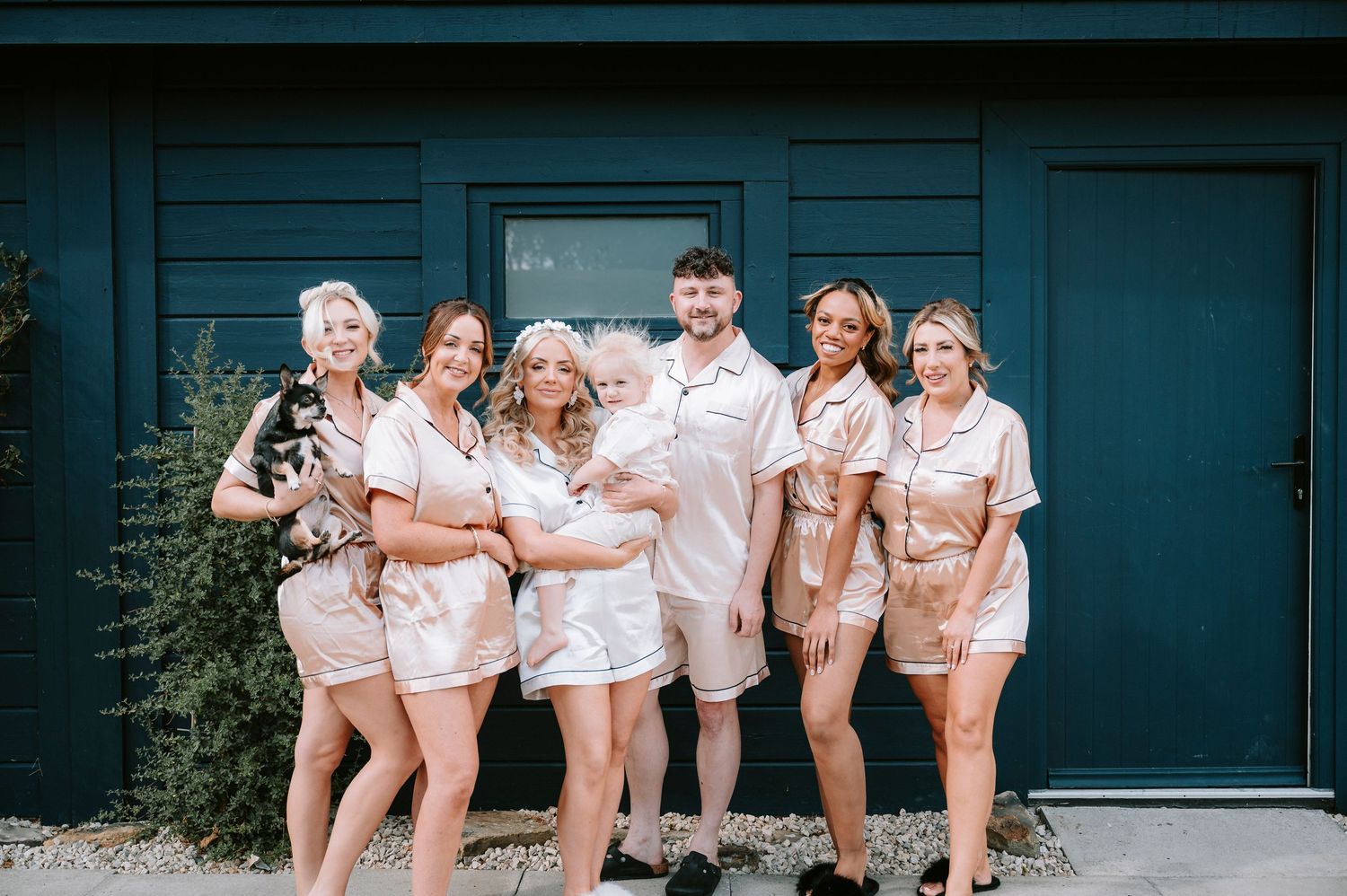 Wedding party in matching robes poses against a dark blue wall during pre-ceremony preparations.