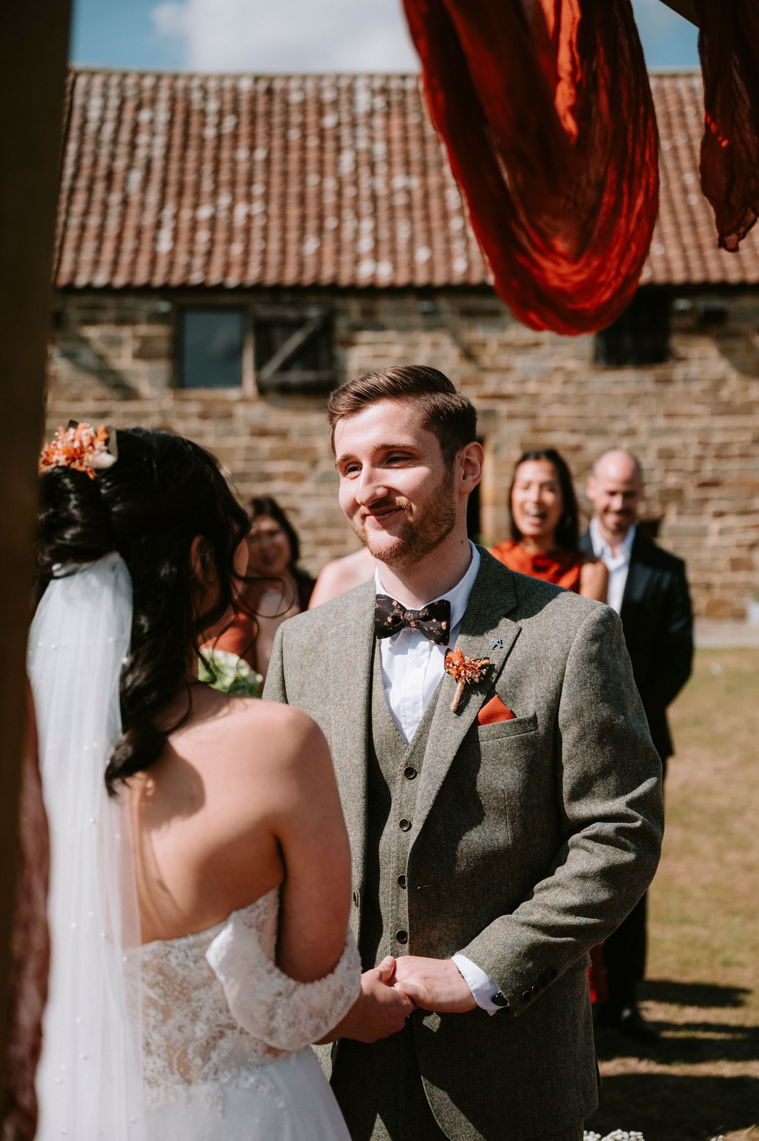 Outdoor wedding ceremony with red drapery and brick architecture in the background.