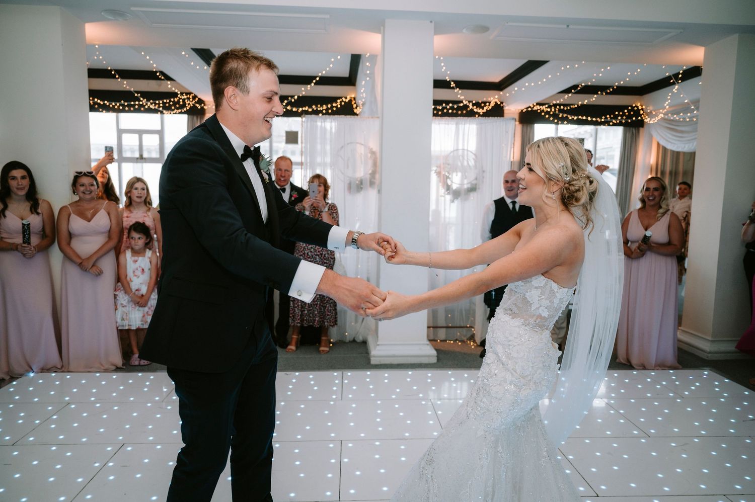 Wedding guests dance and celebrate on an illuminated dance floor at an elegant reception venue.