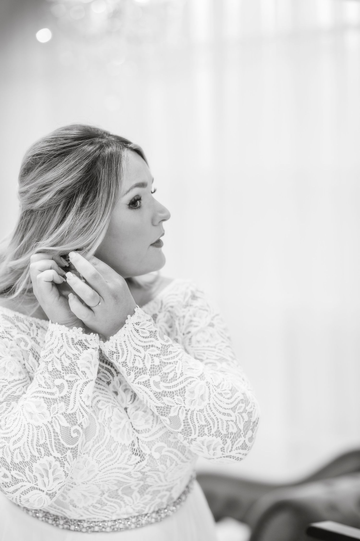 A black and white photo of someone wearing a delicate lace wedding dress while getting ready.