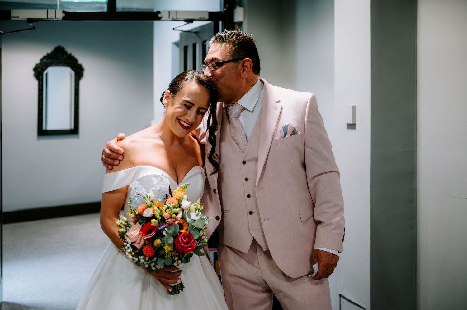 Wedding couple sharing an intimate moment in a hallway, with contrasting white dress and light suit.