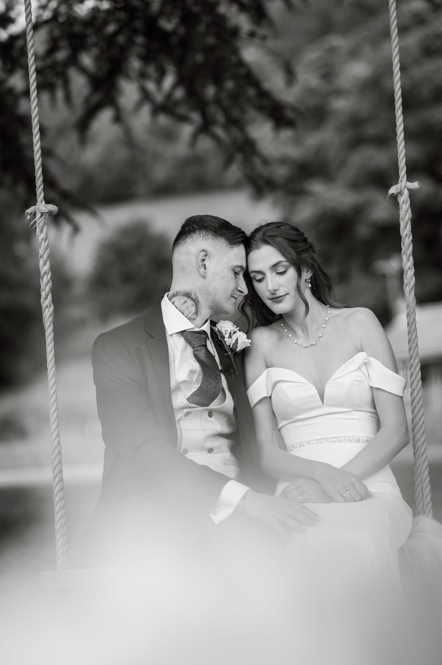 Artistic black and white wedding portraits captured on a swing in a garden setting.