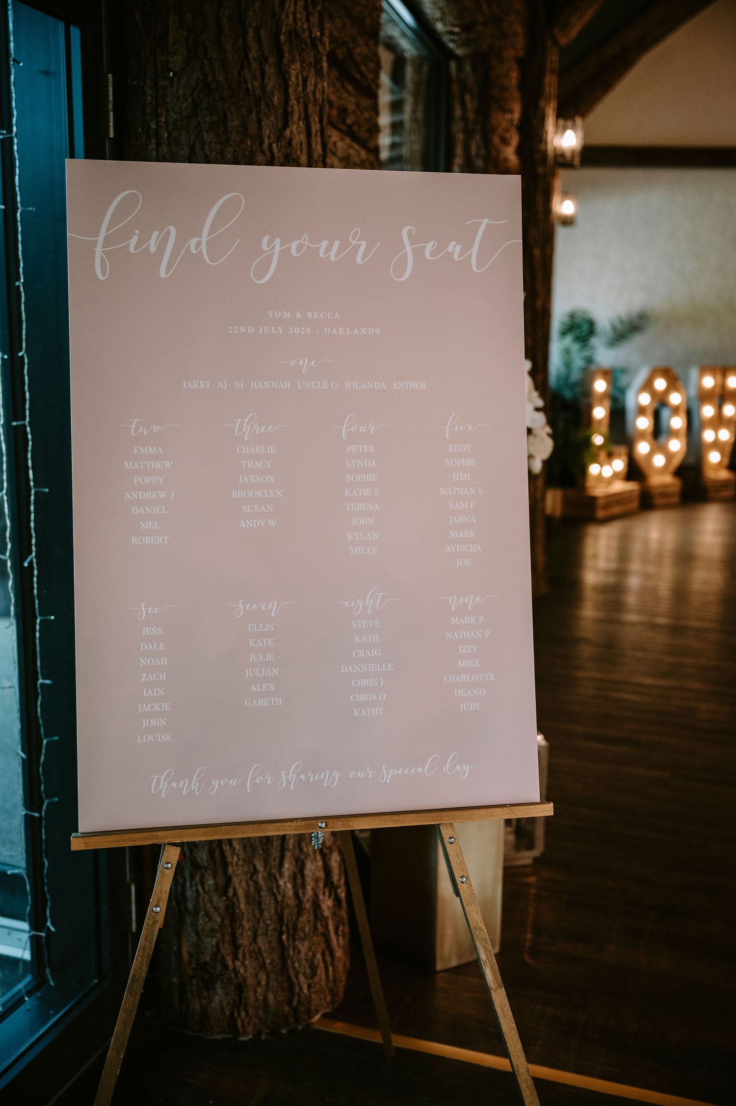 Wedding seating chart displays written in elegant calligraphy on white boards mounted on wooden easels.