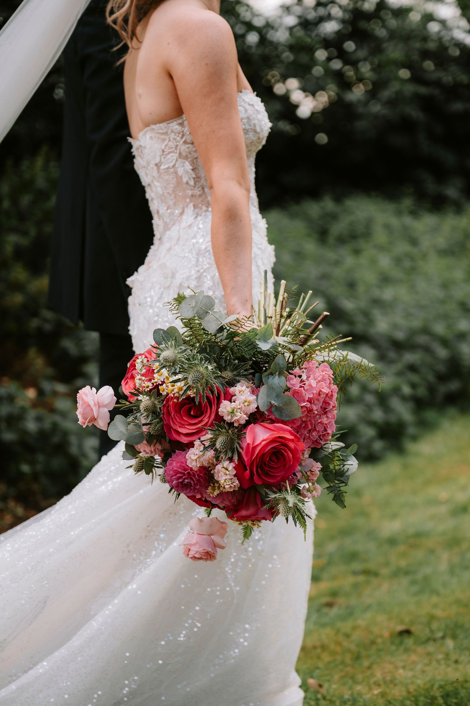 Beautiful wedding bouquet with red roses and pink flowers against a white wedding dress.