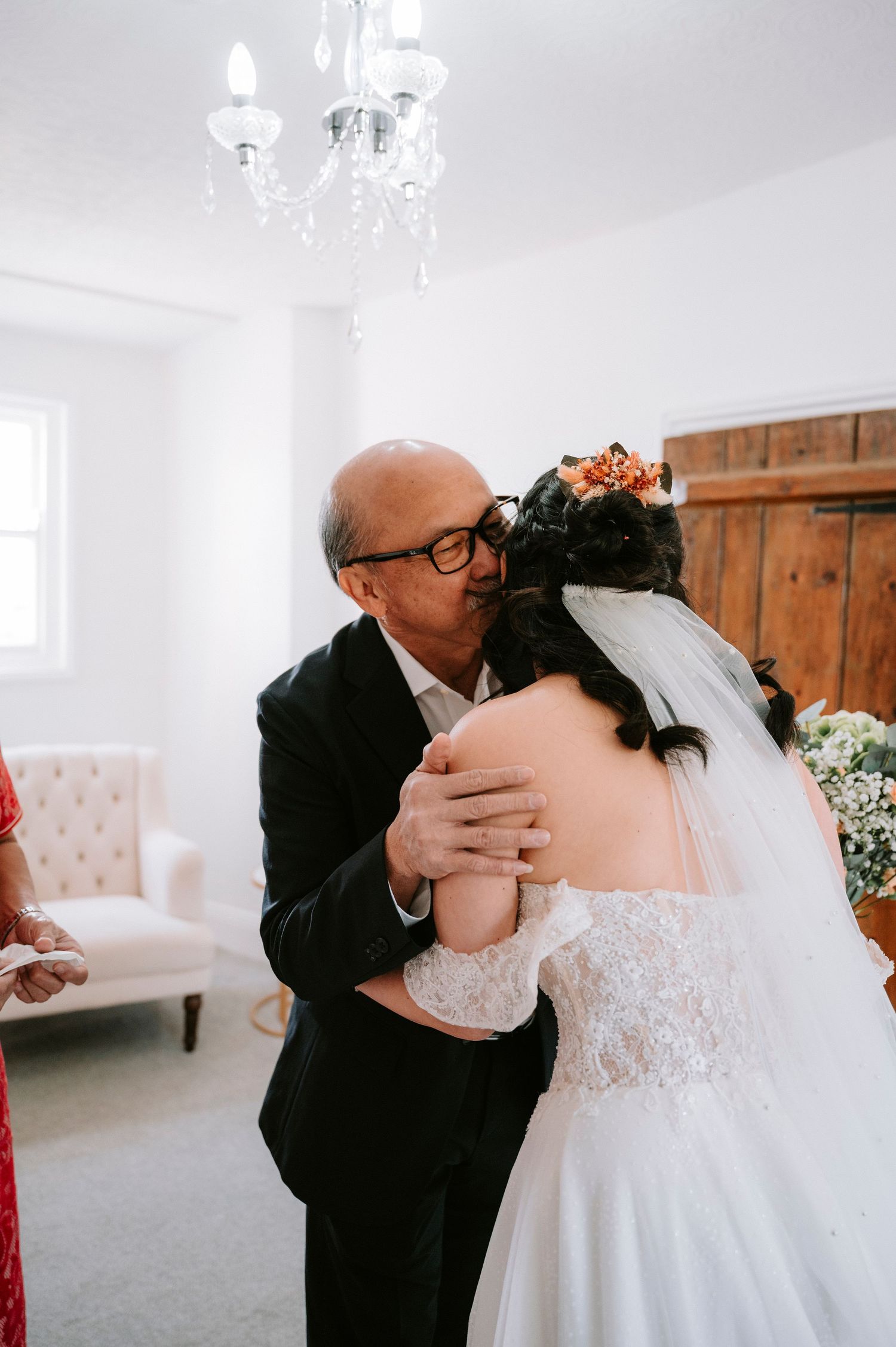 Emotional moment shared between bride in white lace gown and loved one before ceremony.