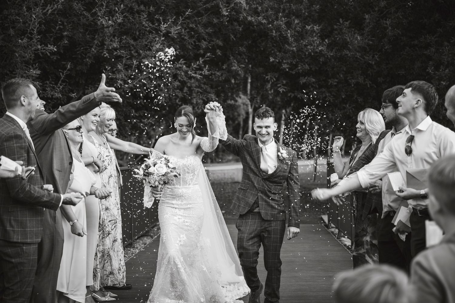 Black and white photo of wedding guests dancing and celebrating at an outdoor reception.