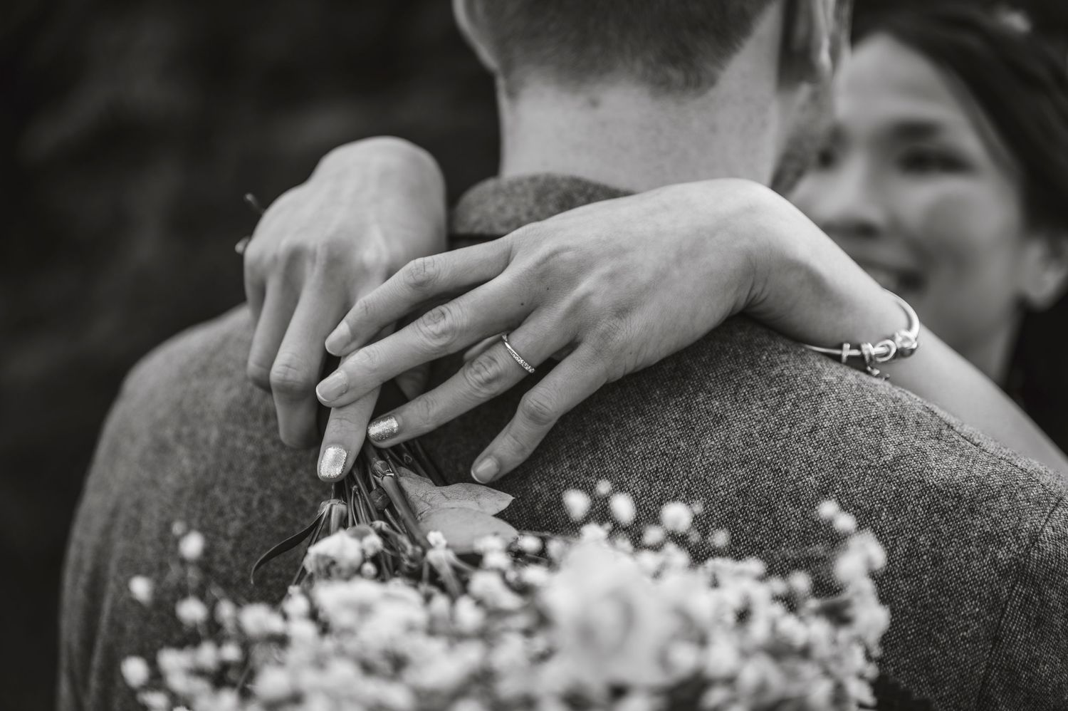 Black and white close-up of hands embracing with baby's breath flowers in a romantic moment.