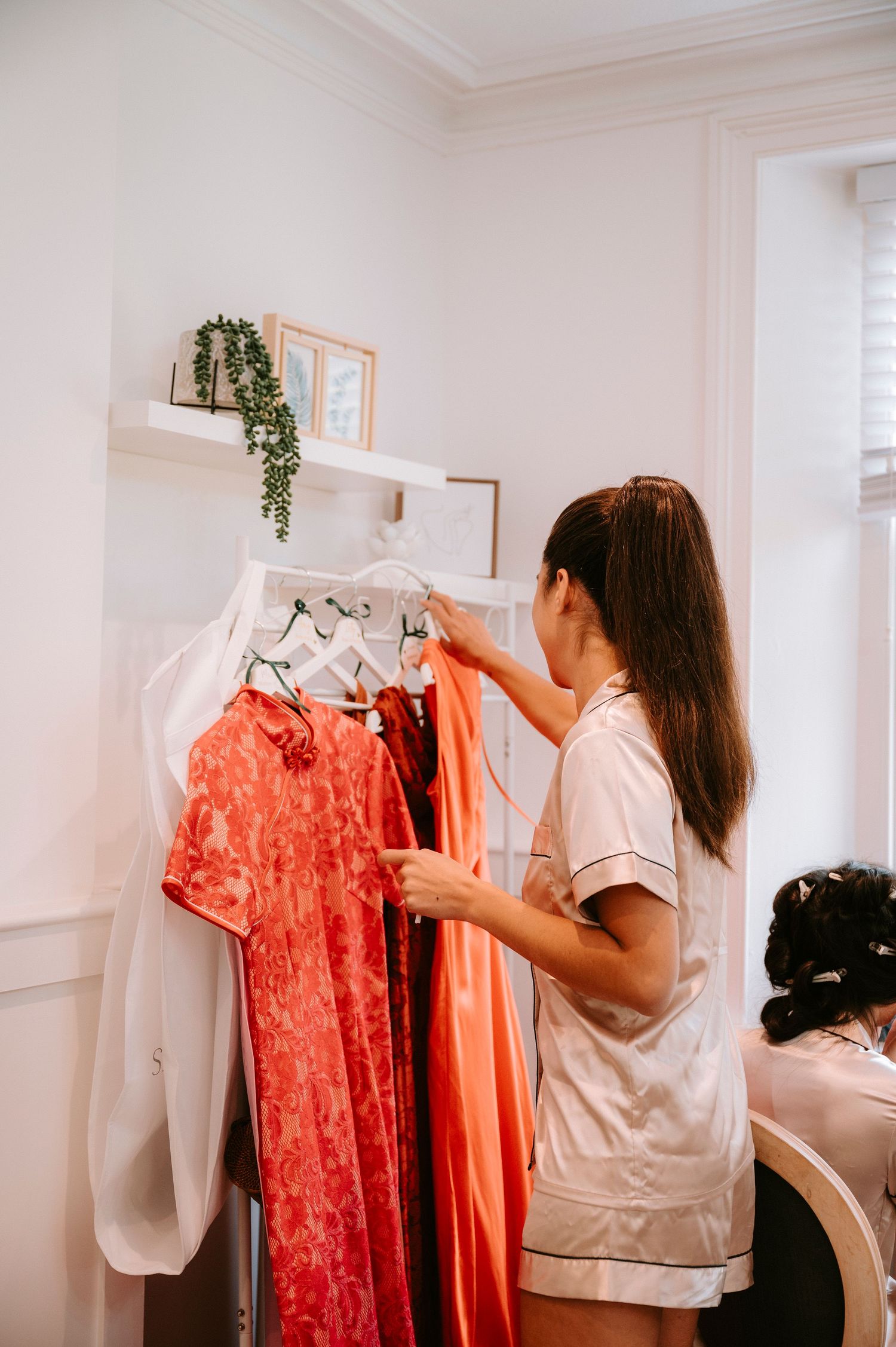 Wedding preparations showing coral and white dresses hanging in bright room.