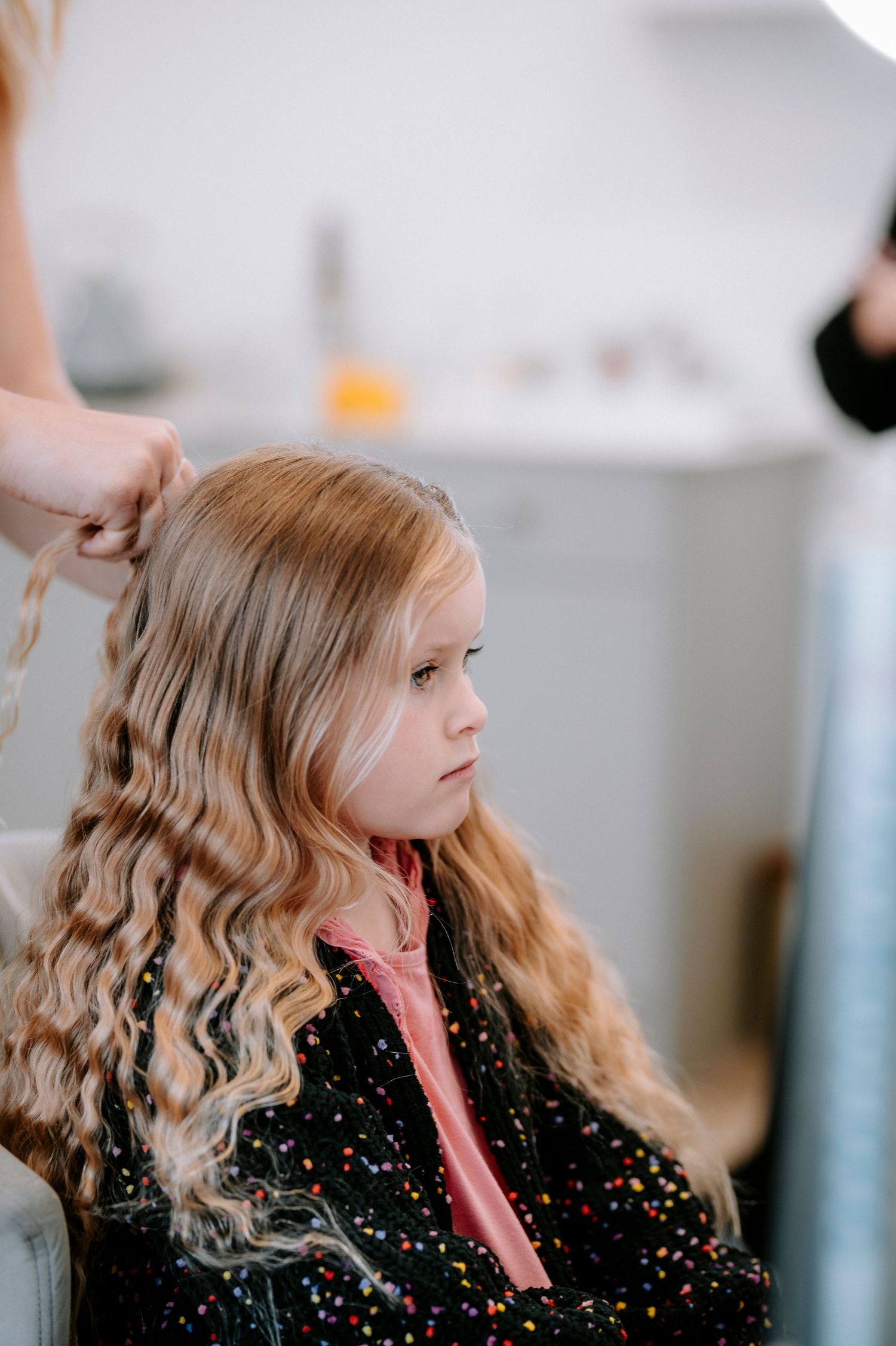 Close up of curled blonde hair being styled with a pink curling iron.
