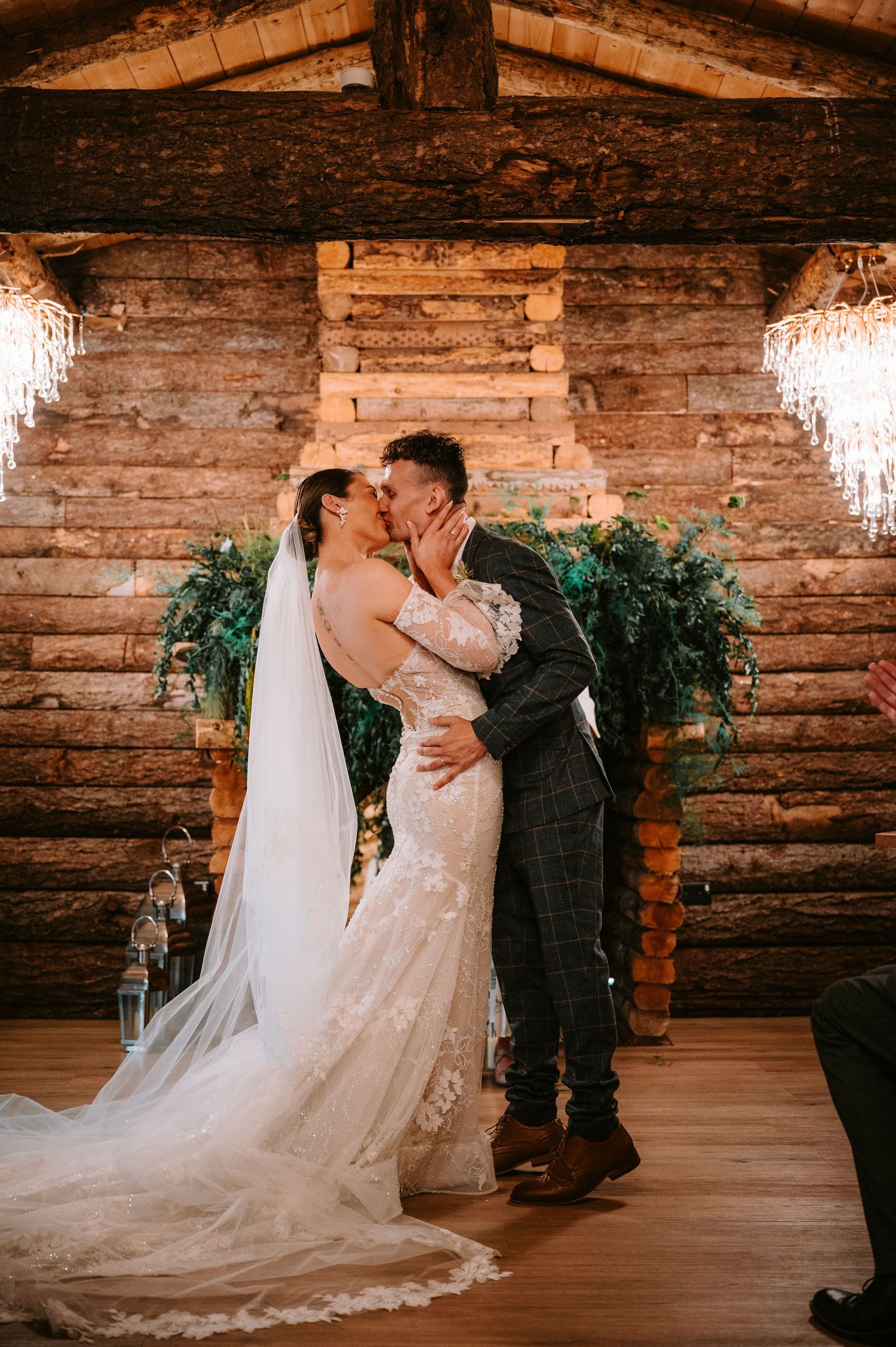 Romantic wedding couple sharing an intimate moment in a rustic wooden barn with crystal chandeliers.