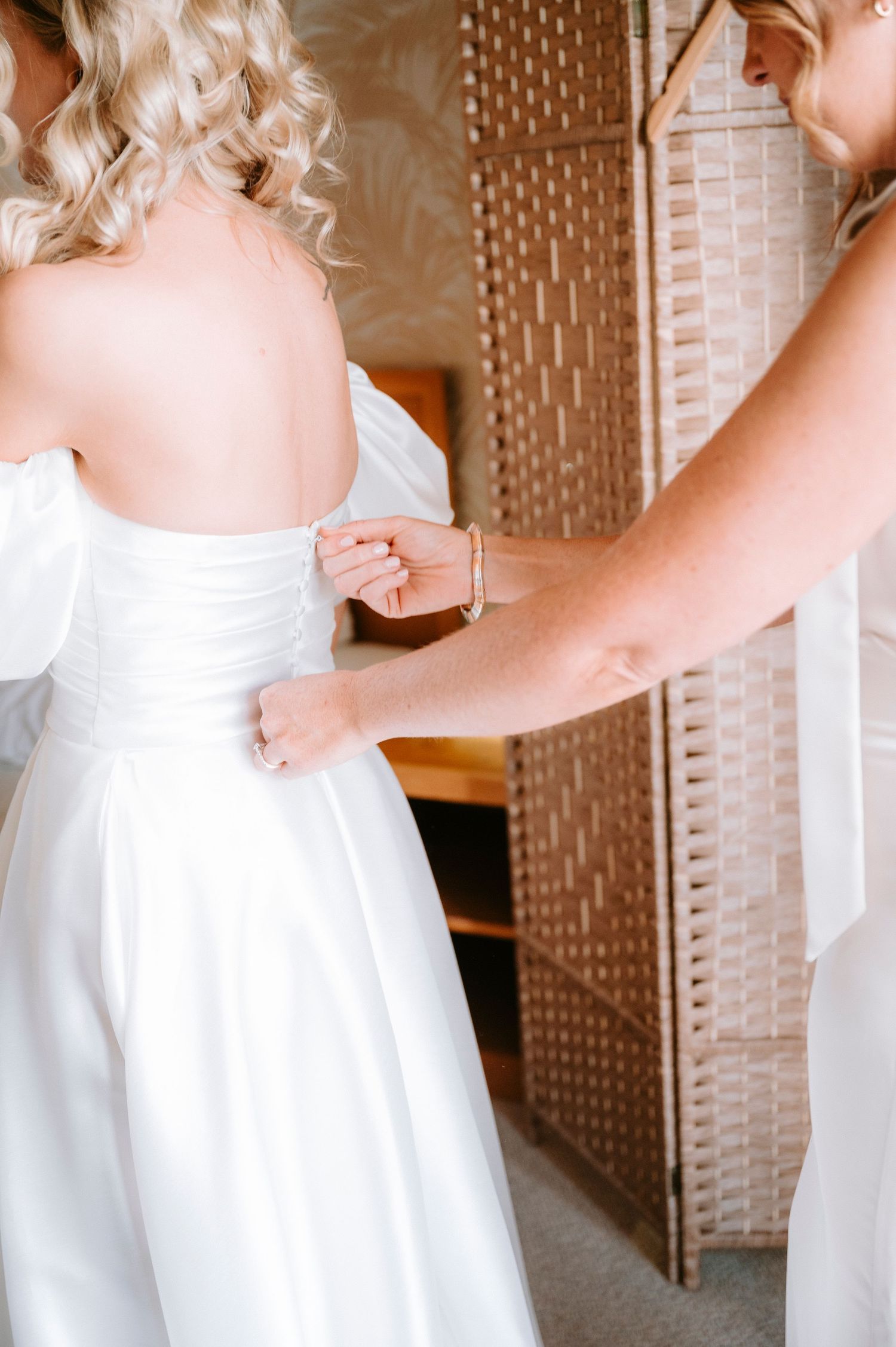 Close-up details of a white wedding dress being adjusted during bridal preparations.
