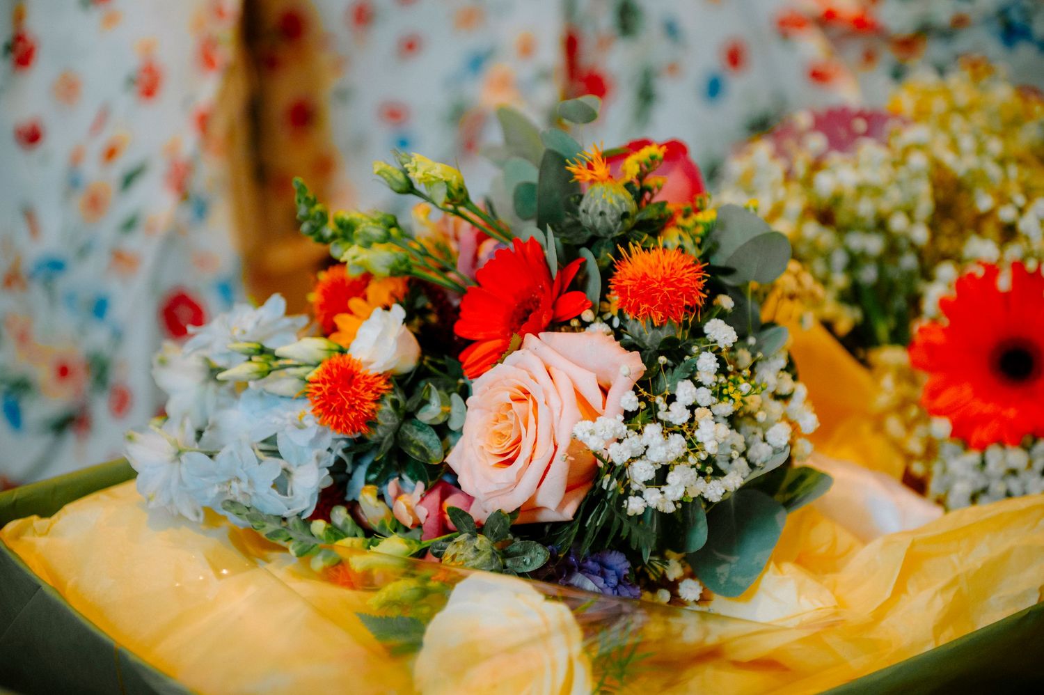 Colorful wedding bouquet with red and peach roses against a blue background.