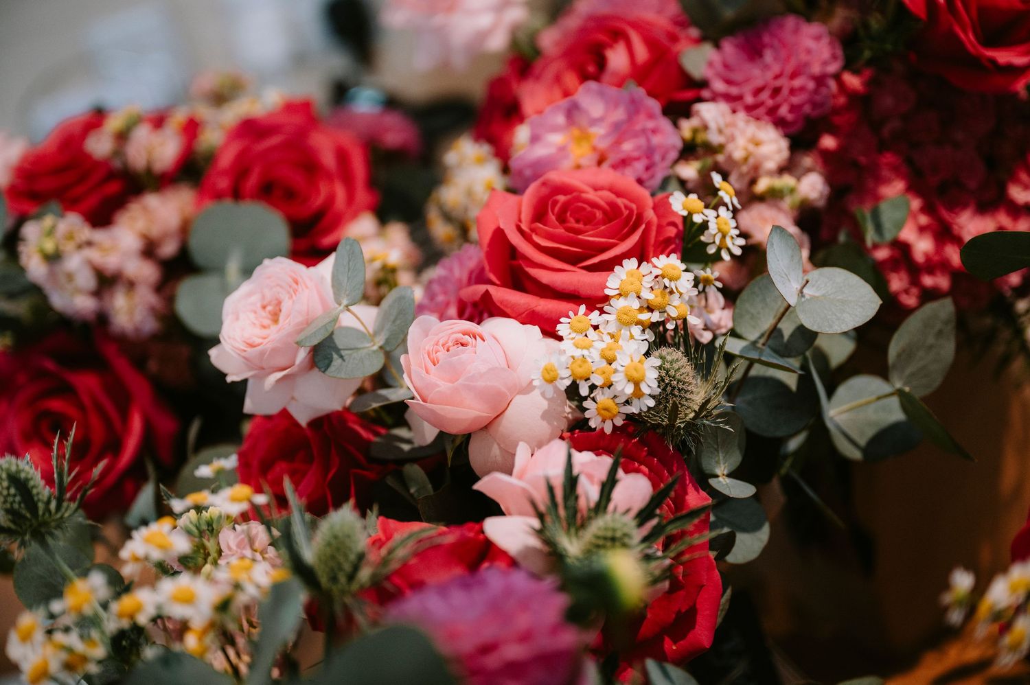 Close-up of vibrant red and pink wedding flowers with eucalyptus accents.