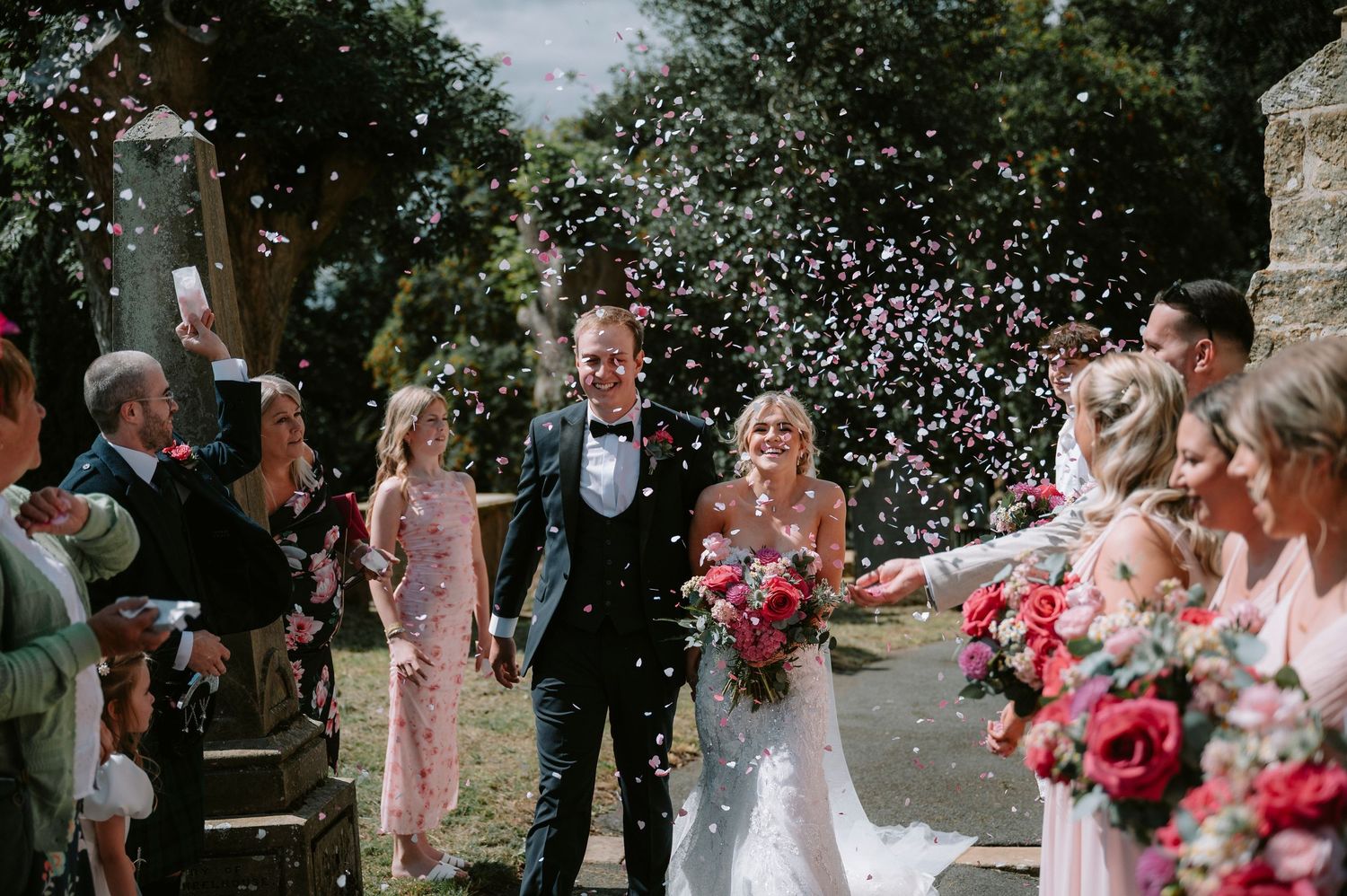 Wedding guests shower the newlyweds with confetti during an outdoor celebration.