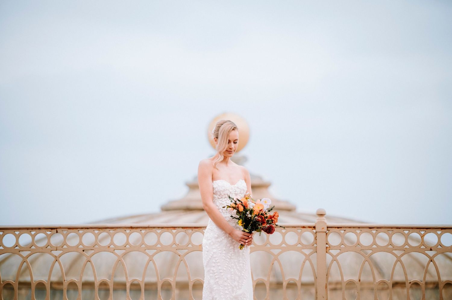 A dreamy bridal portrait captured against a soft blue sky and decorative railing.
