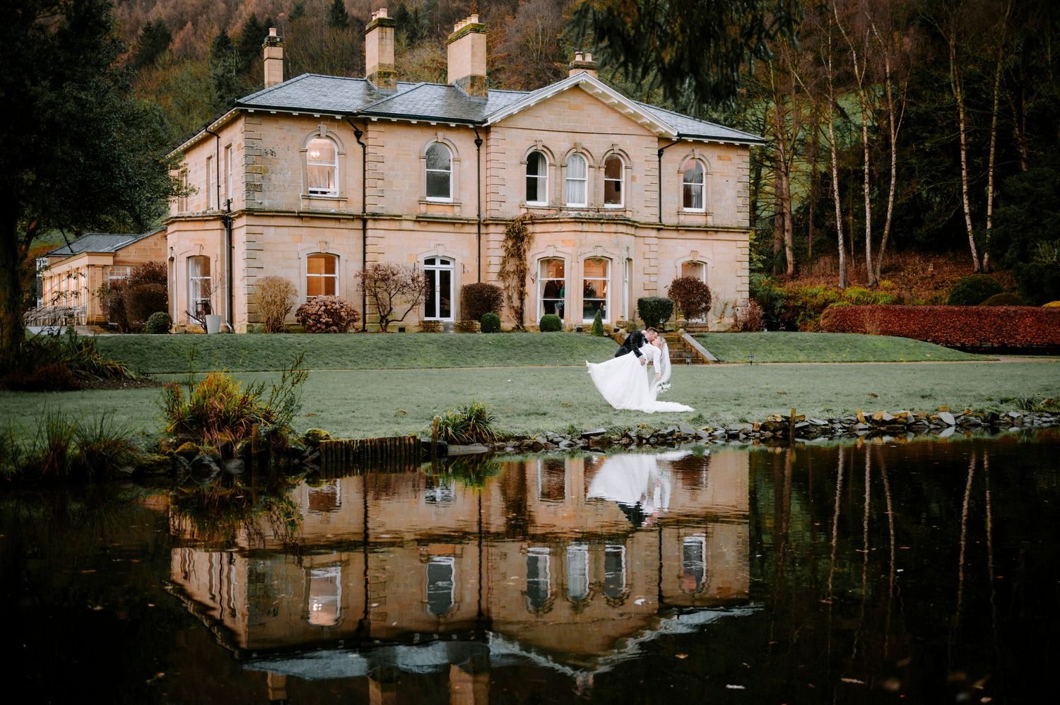Panoramic view of a historic mansion with its reflection in a serene pond.