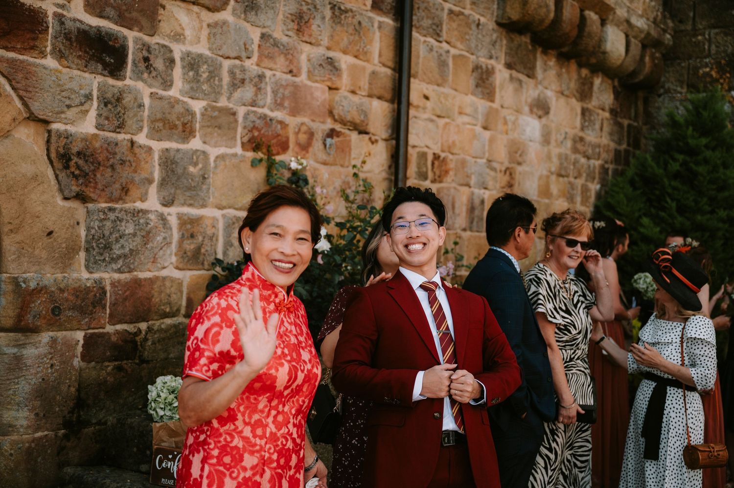 Wedding guests in formal attire celebrating against stone wall backdrop.