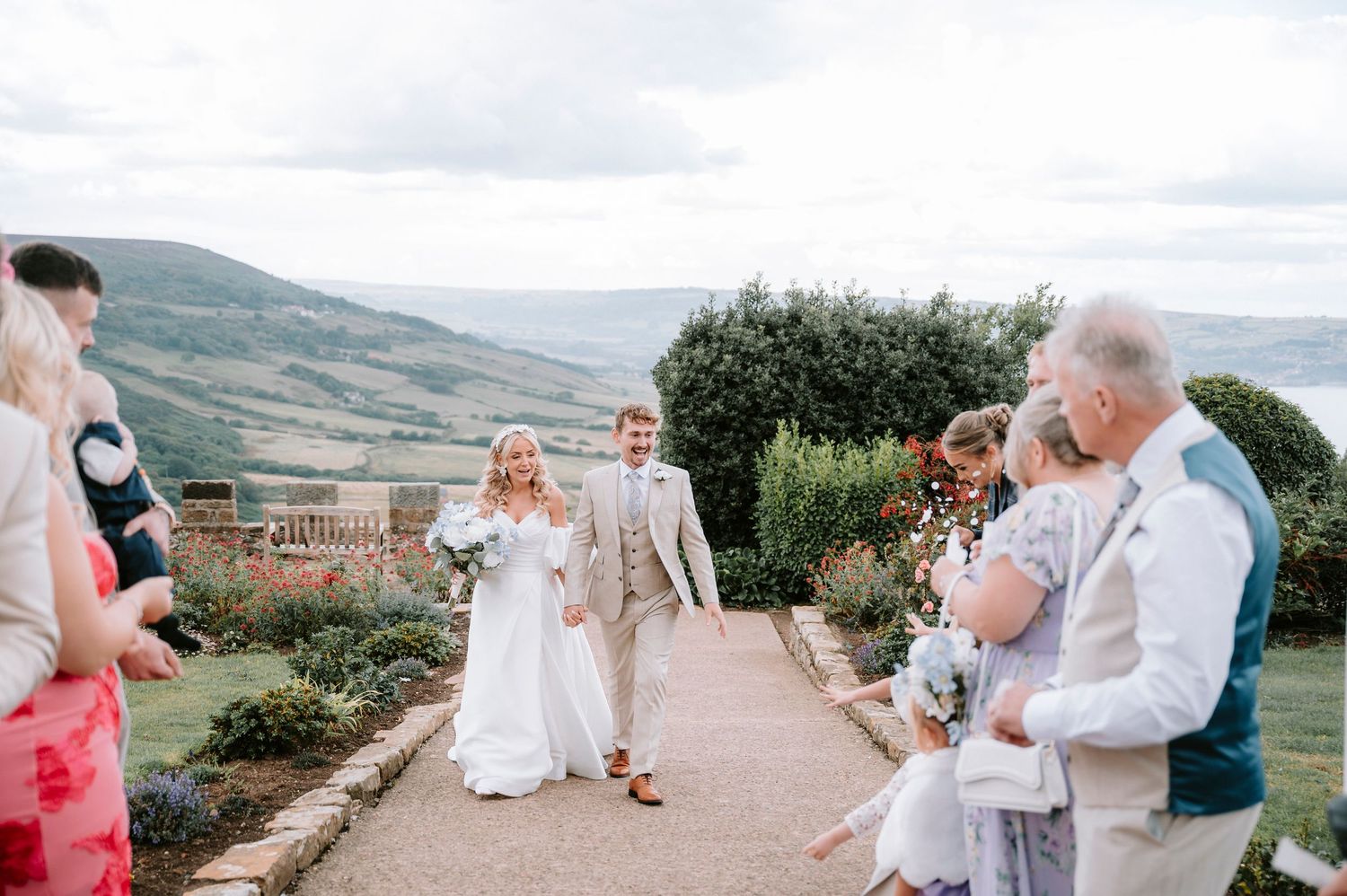 Wedding party poses for photos on a scenic hilltop overlooking a beautiful mountain landscape.