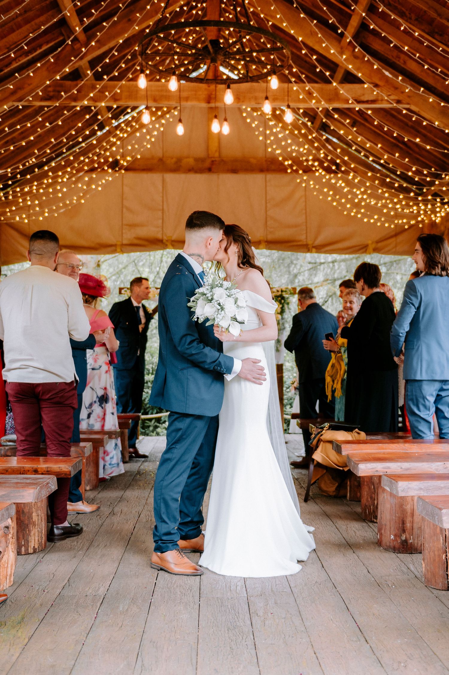 Rustic barn wedding venue with wooden benches and romantic string light decorations.