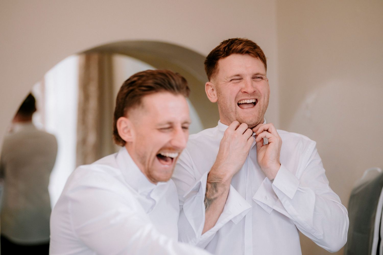 Groomsmen in white dress shirts share laughs and smiles during wedding day preparations.