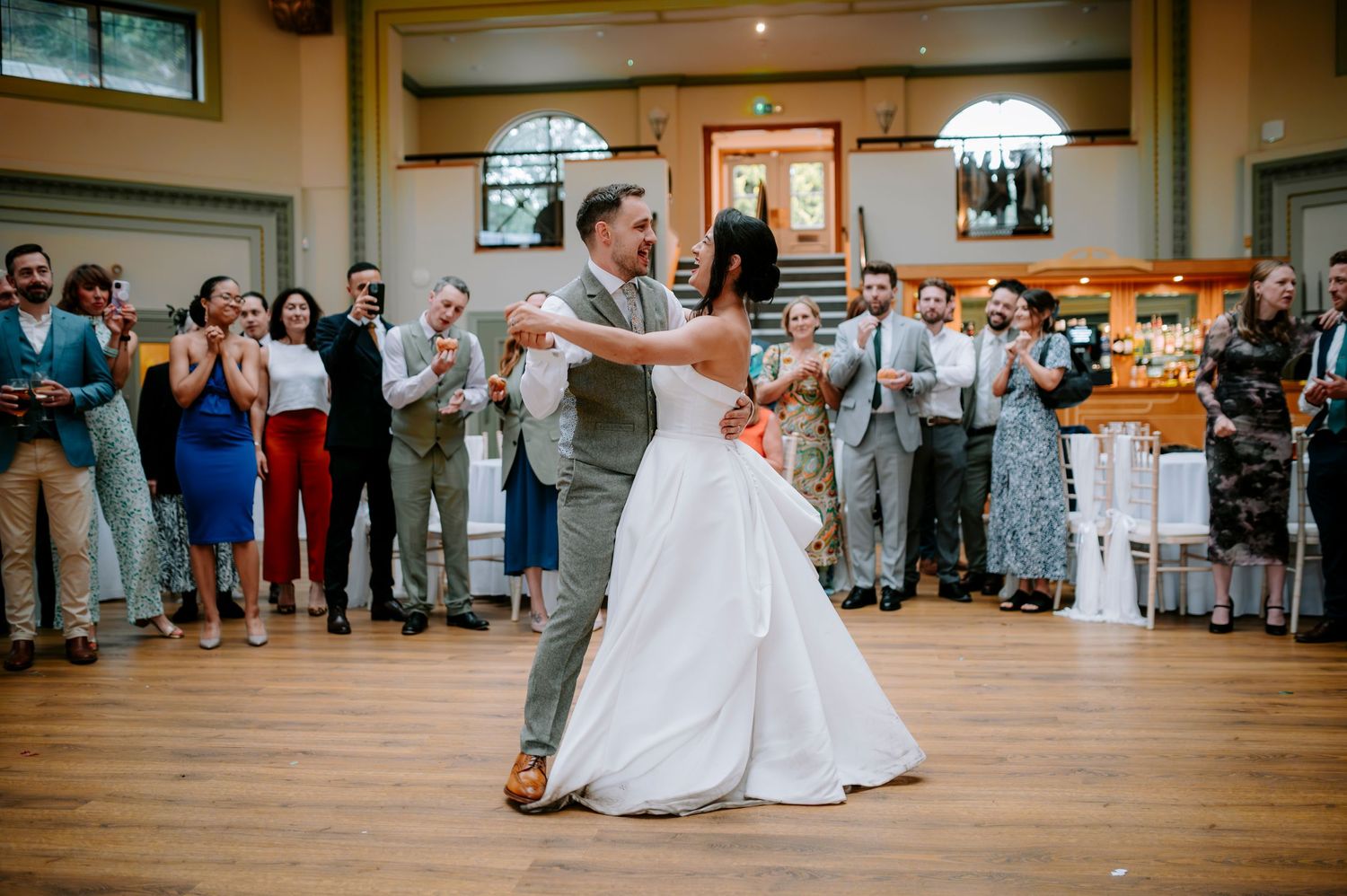 A couple shares an energetic dance moment at their wedding reception surrounded by cheering guests.