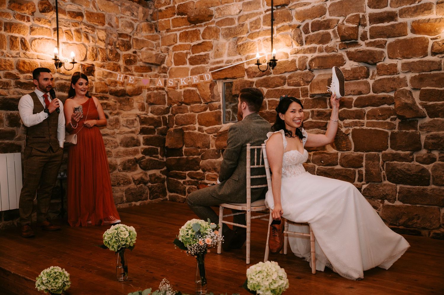 Elegant wedding reception setup in a historic stone building with floral centerpieces and wooden chairs.