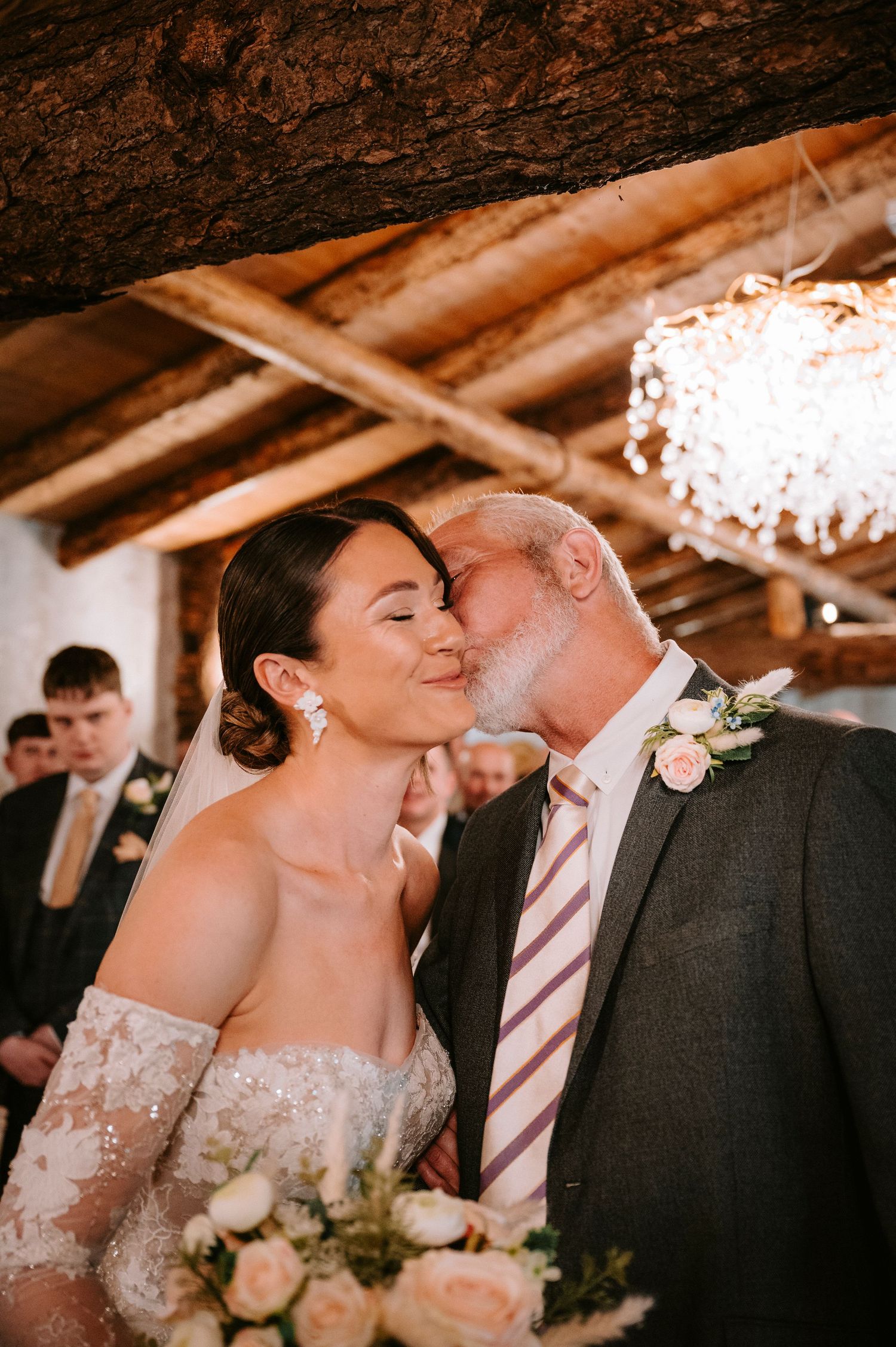 Romantic moment captured under rustic wooden beams at an indoor wedding venue.