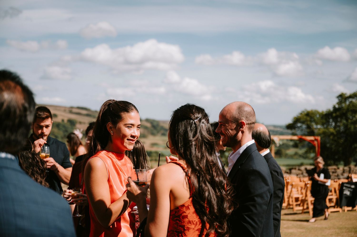 Wedding guests mingling outdoors at a sunny countryside celebration.