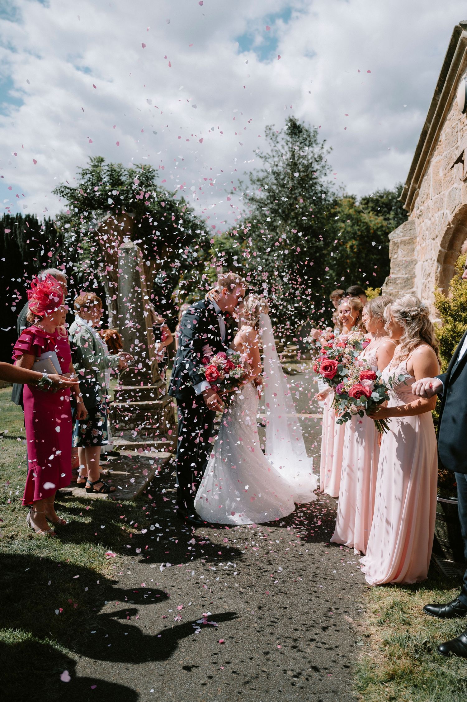 Wedding celebration with bridesmaids in pink dresses throwing confetti in the air.