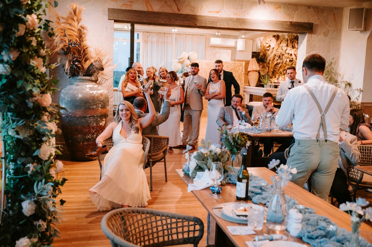 Wedding reception celebration in a rustic venue decorated with floral arrangements and twinkling lights.