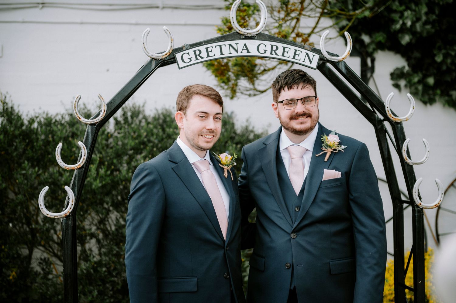 Two people in suits standing under the Gretna Green horseshoe arch.