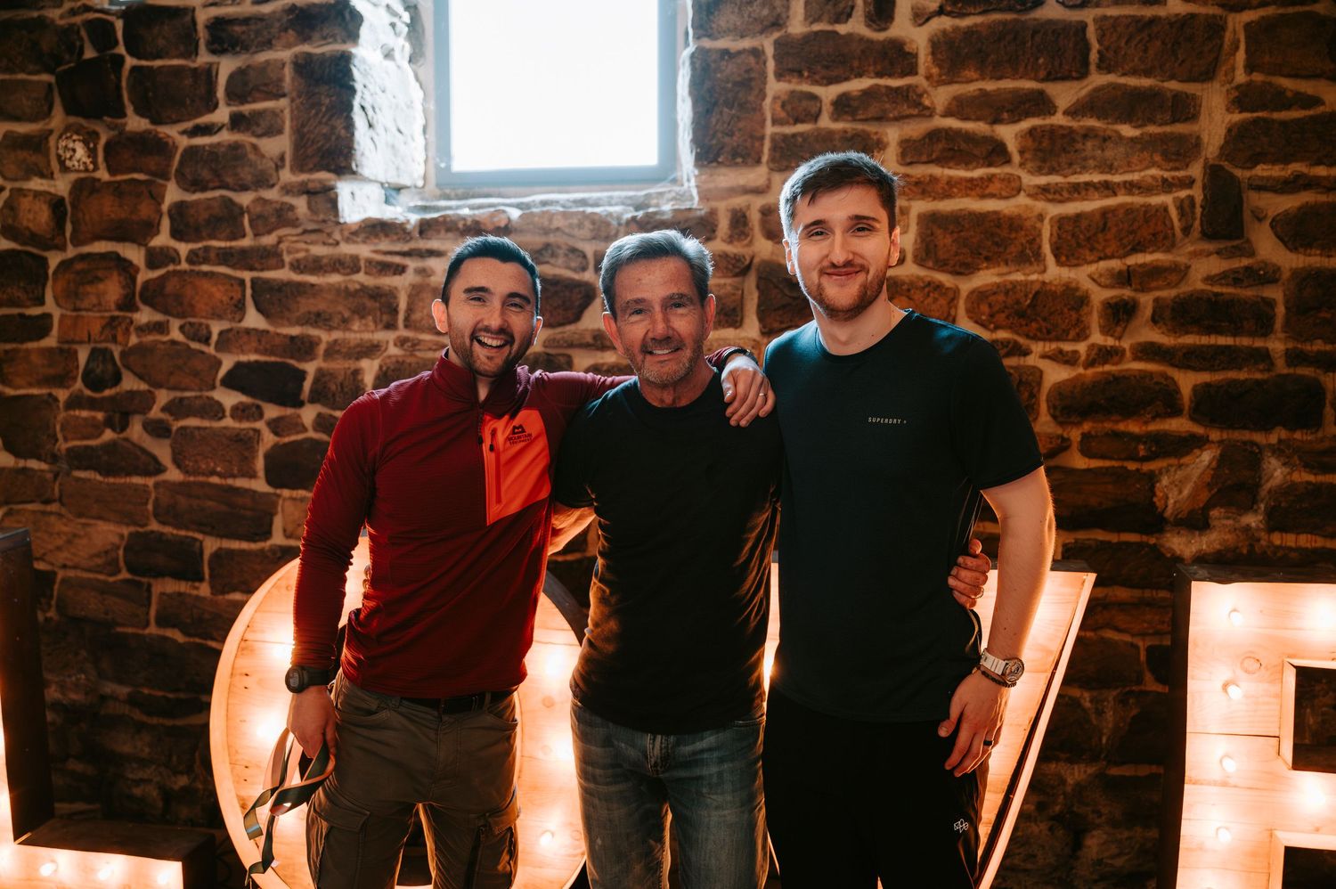 Group photo in front of rustic stone wall with ambient lighting.