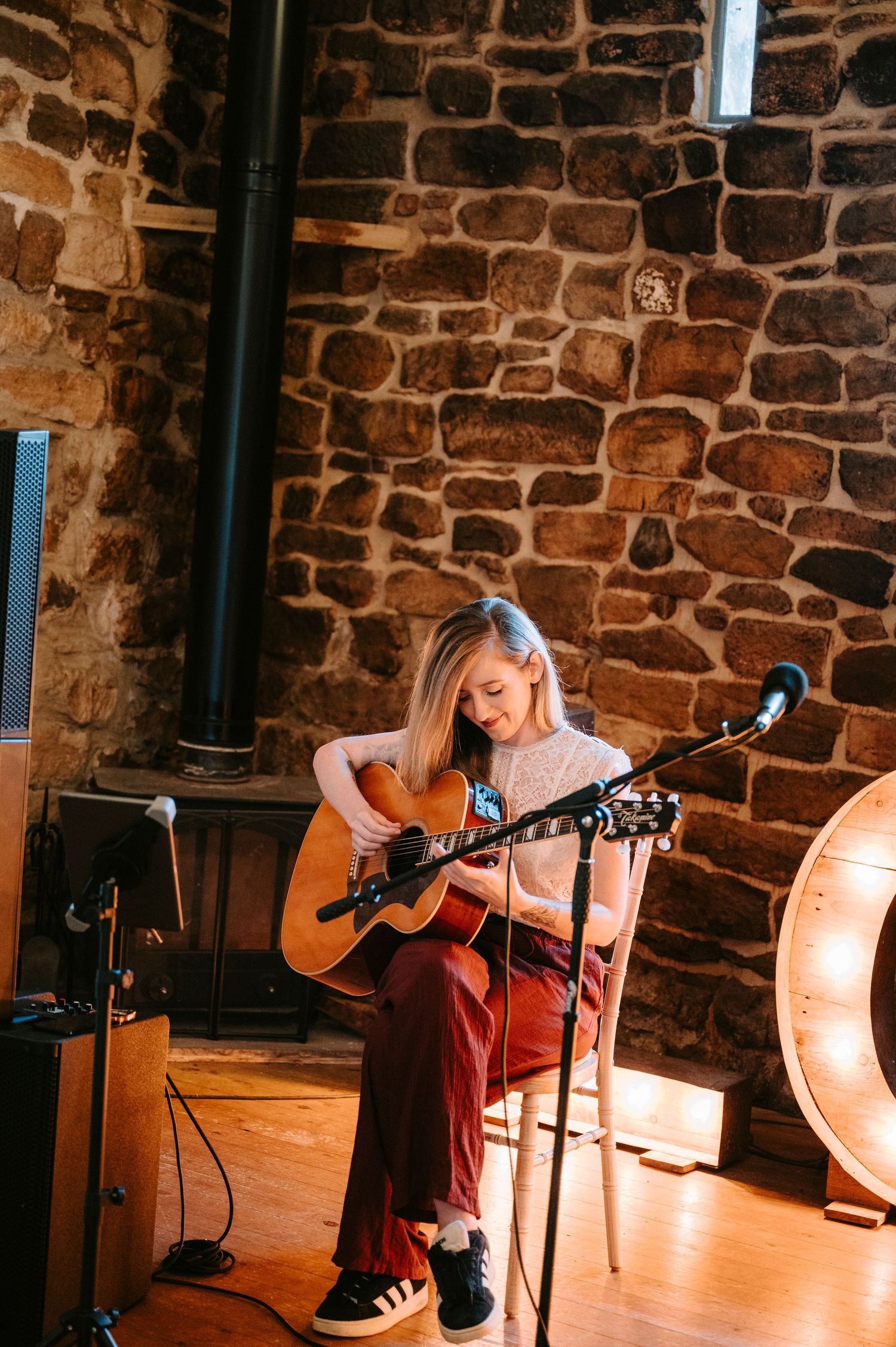 Musician performs with acoustic guitar in rustic stone-walled venue with warm lighting.