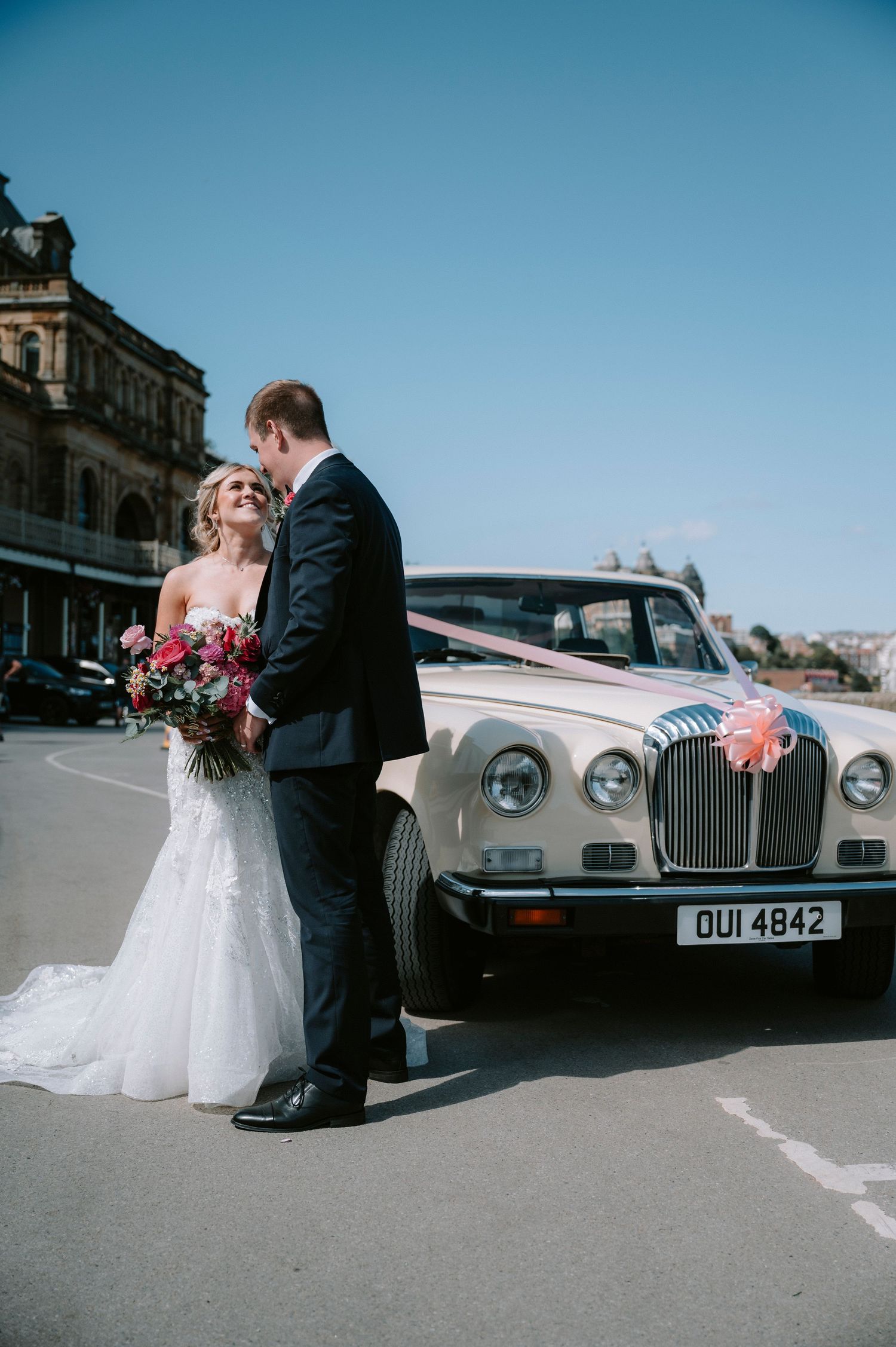 Classic vintage wedding car parked on a street with a romantic couple posing nearby.