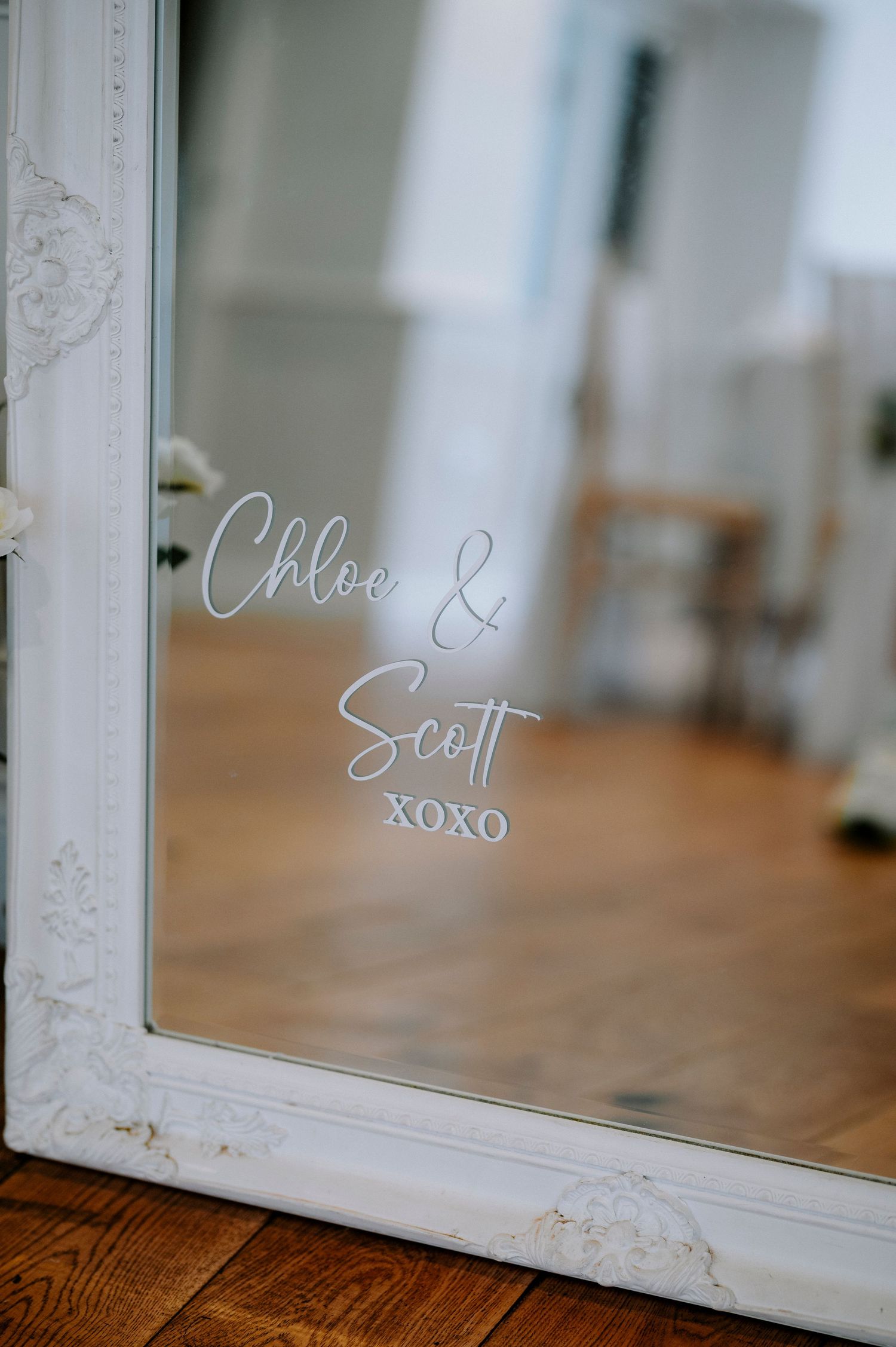 White ornate vintage frame with handwritten text on glass sitting on wooden surface.