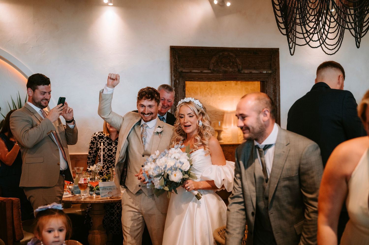A group of wedding guests dancing and celebrating at an indoor reception with warm lighting and elegant decor.