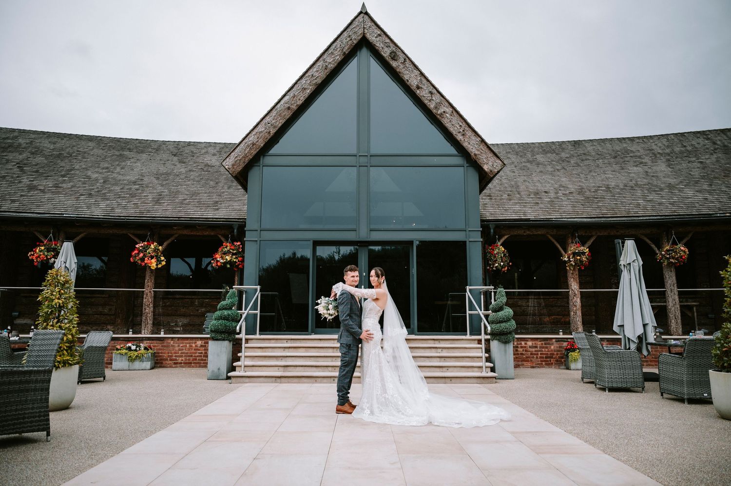 A couple stands outside a modern lodge-style venue with glass windows and stone accents on their wedding day.