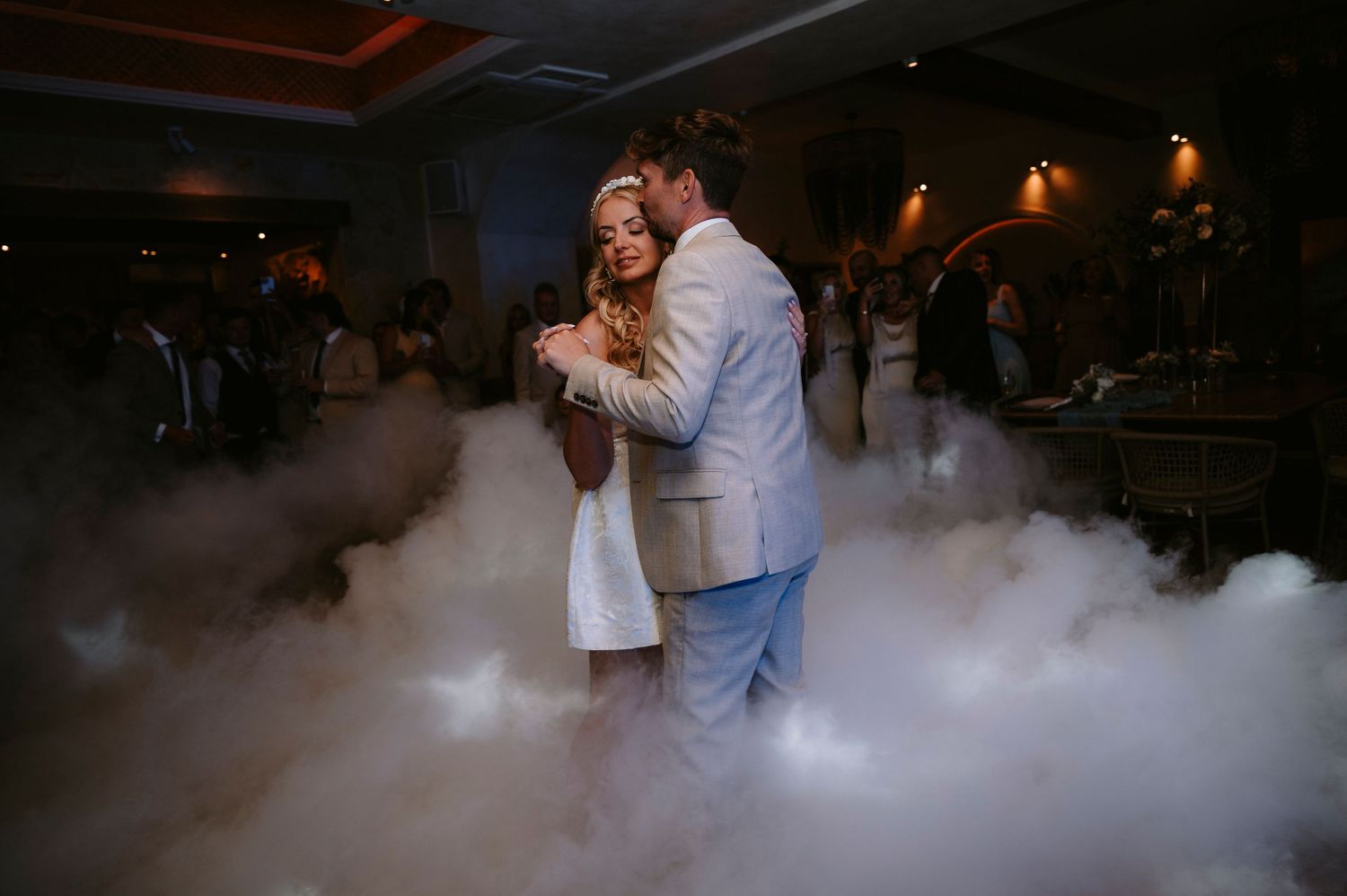 Couple dancing surrounded by atmospheric fog effects at their wedding reception.