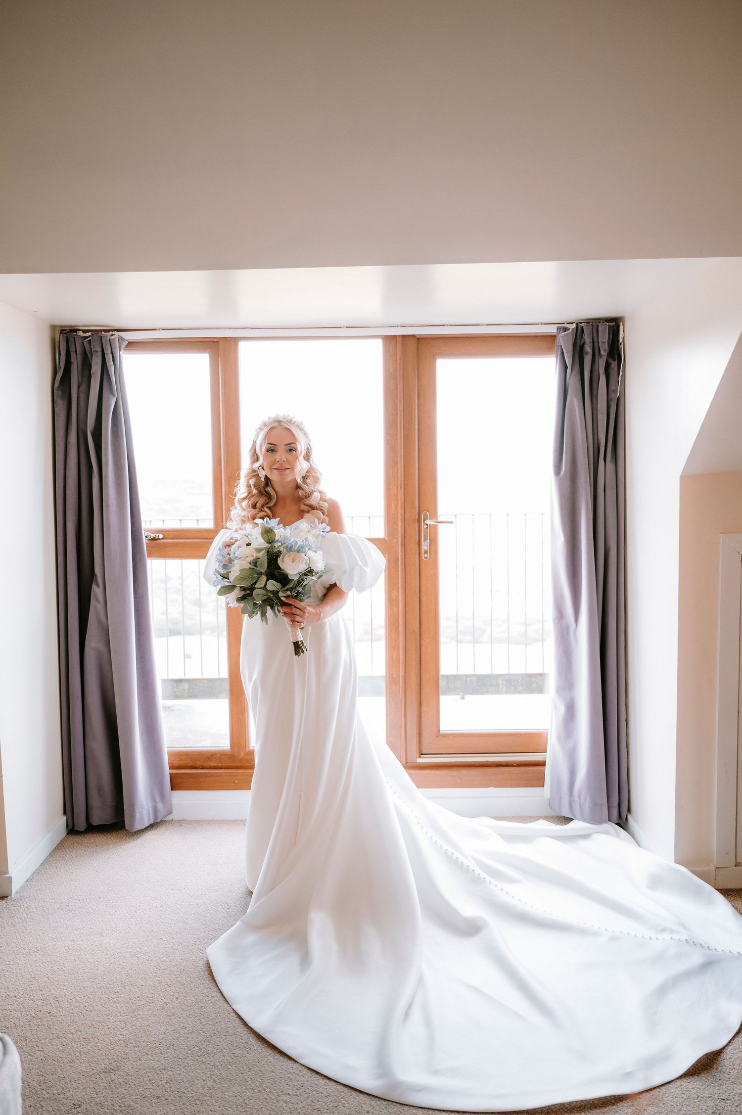 Elegant wedding dress flowing across a sunlit room with window views.