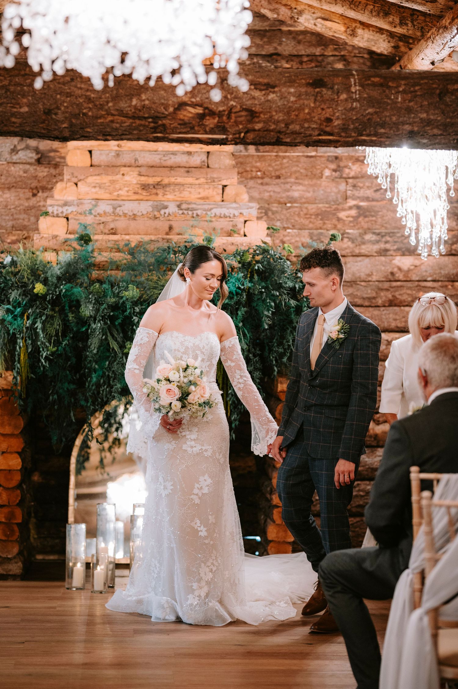 Bride in lace gown and groom in plaid suit during their rustic barn wedding ceremony.