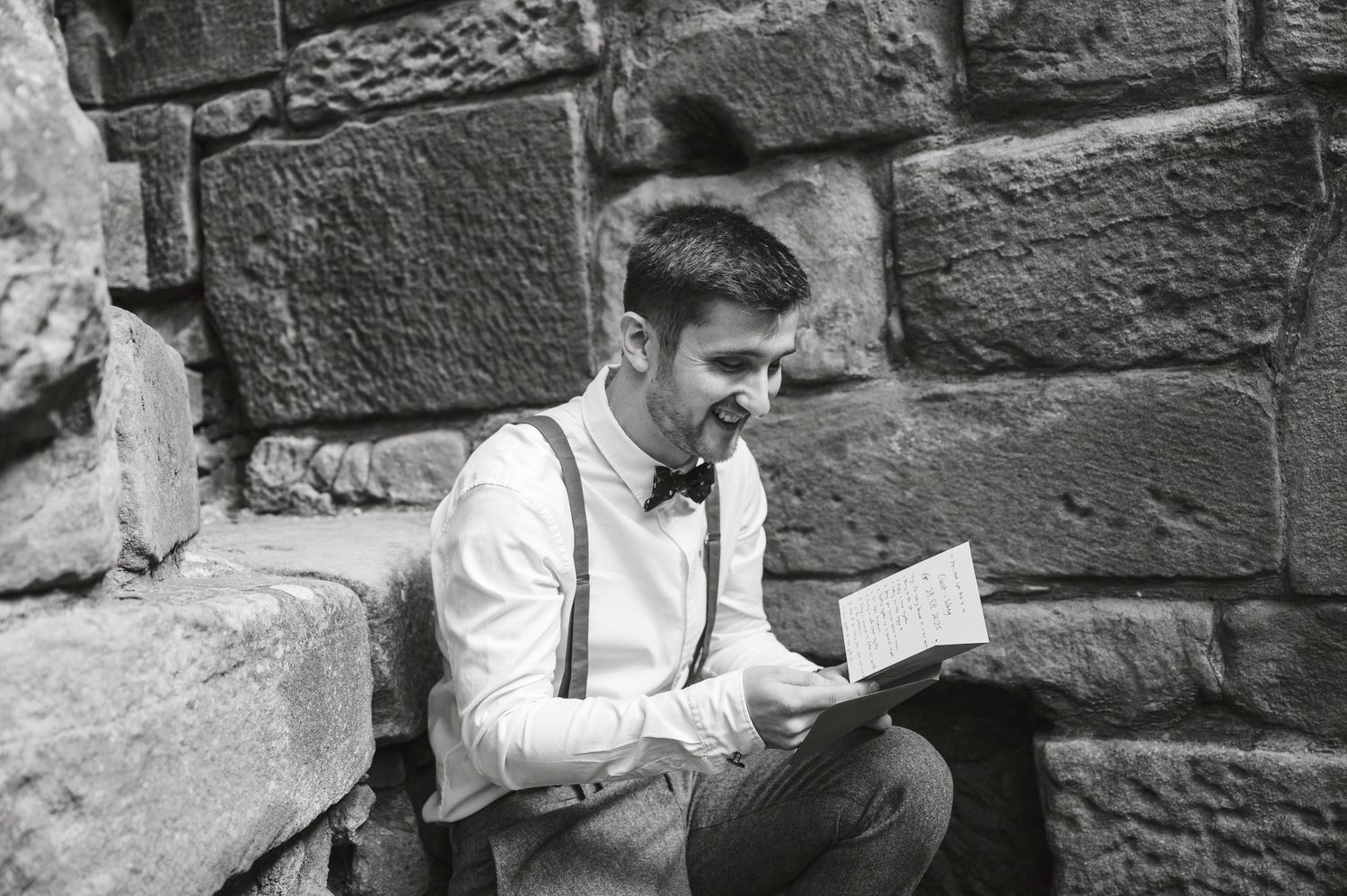 Black and white photo of people sitting against stone wall texture.