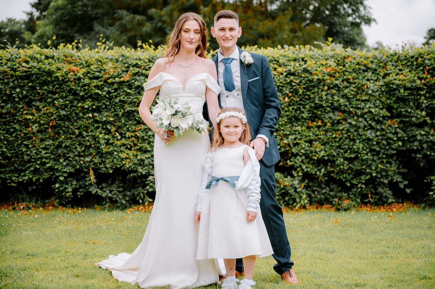 Wedding party gathers on a lawn with elegant floral arrangements and greenery.