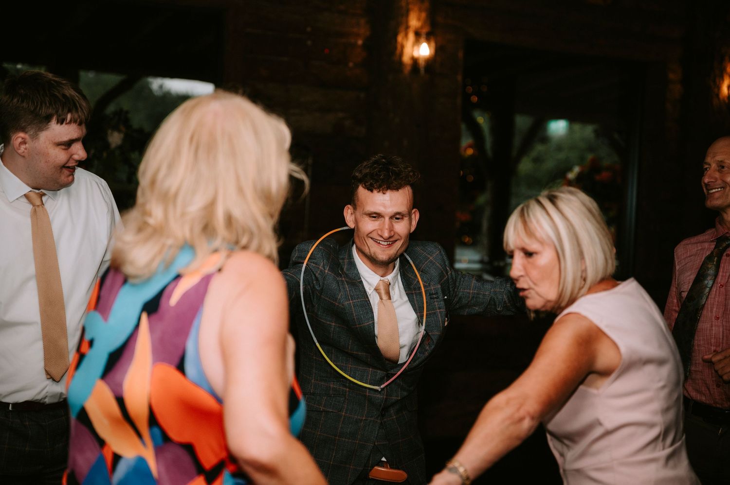 Wedding guests dancing and celebrating at an indoor reception with warm lighting.