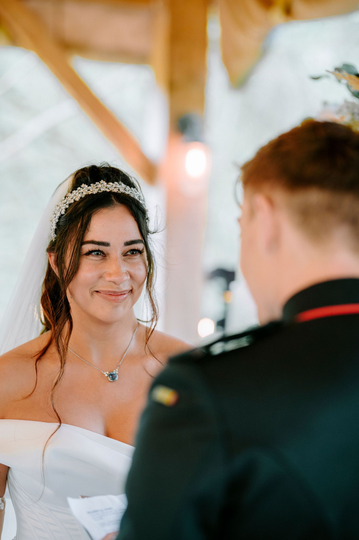 Bride wearing a delicate crystal headpiece and off-shoulder wedding gown smiles during the ceremony.