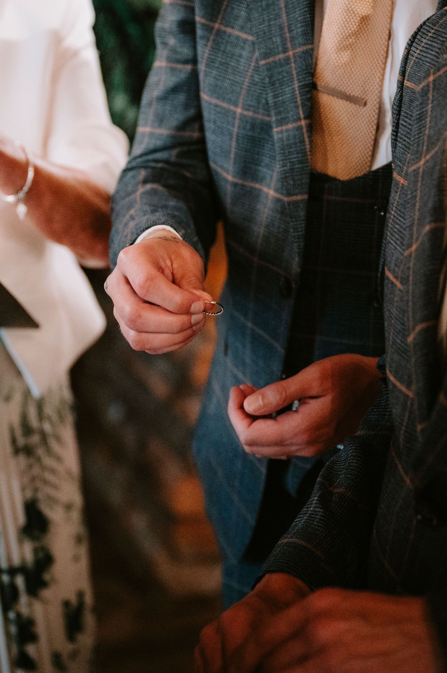 Close-up of hands wearing a plaid suit jacket during a wedding ceremony.