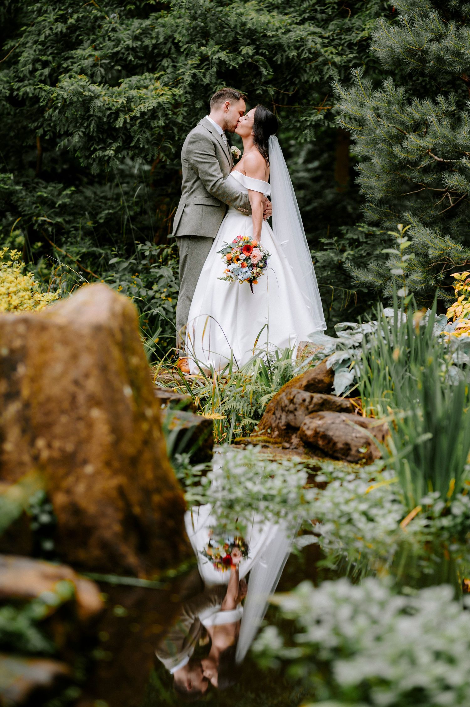 Wedding couple photographed with creative reflection in garden water feature.