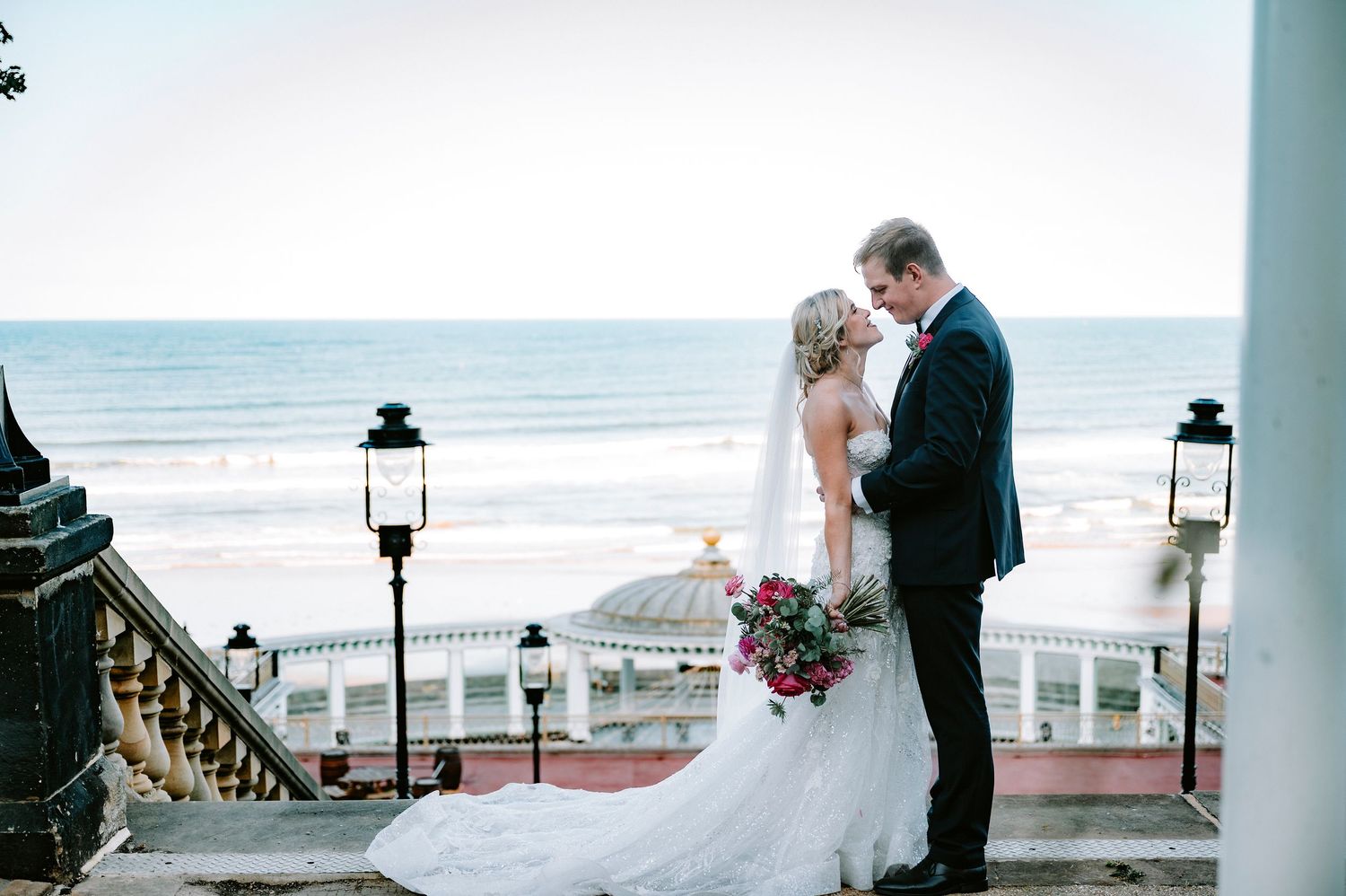 Elegant wedding couple shares intimate moments along a beachfront promenade with ocean views.
