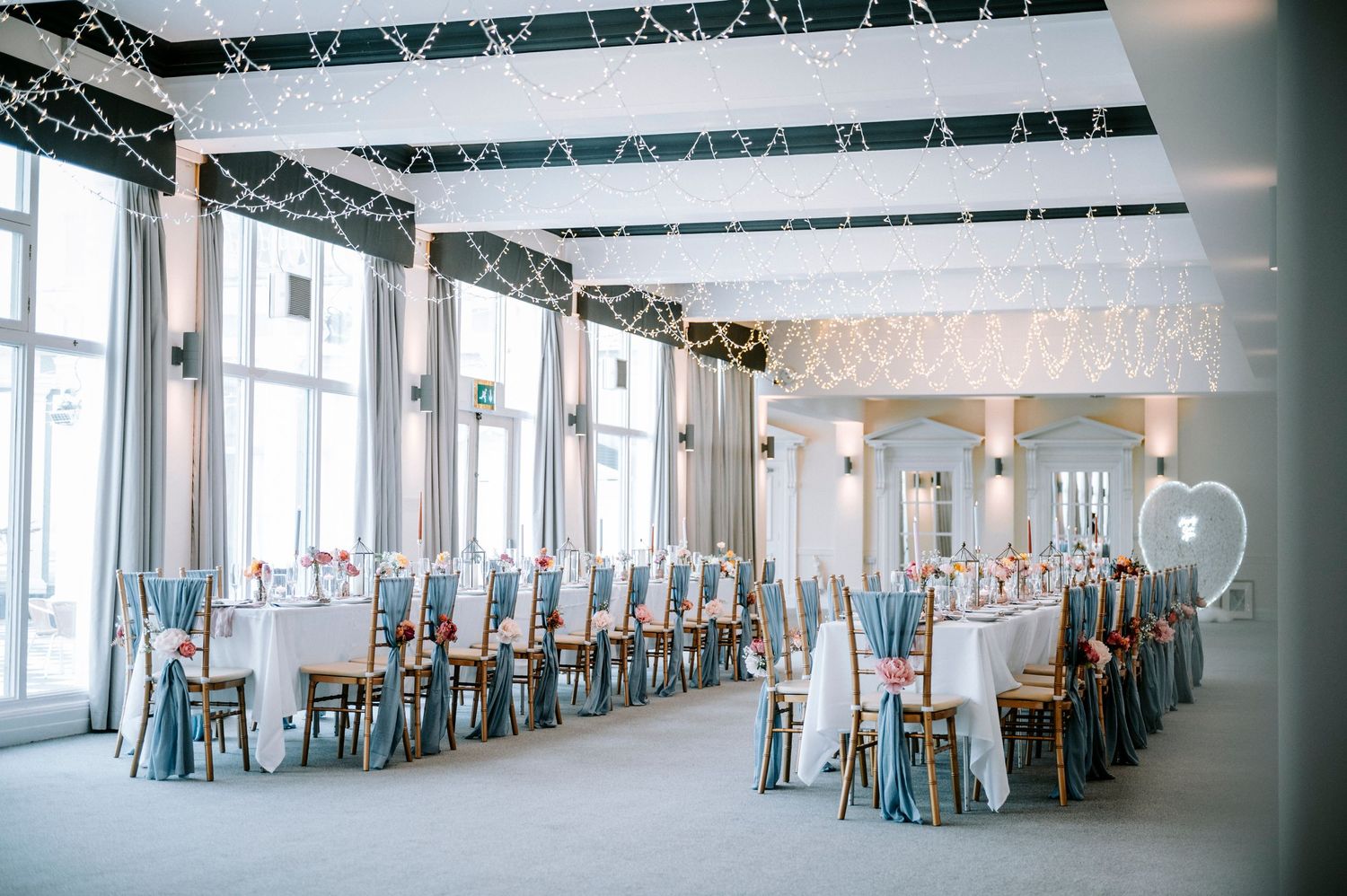 Panoramic view of an empty wedding reception venue with white tables and blue chairs.